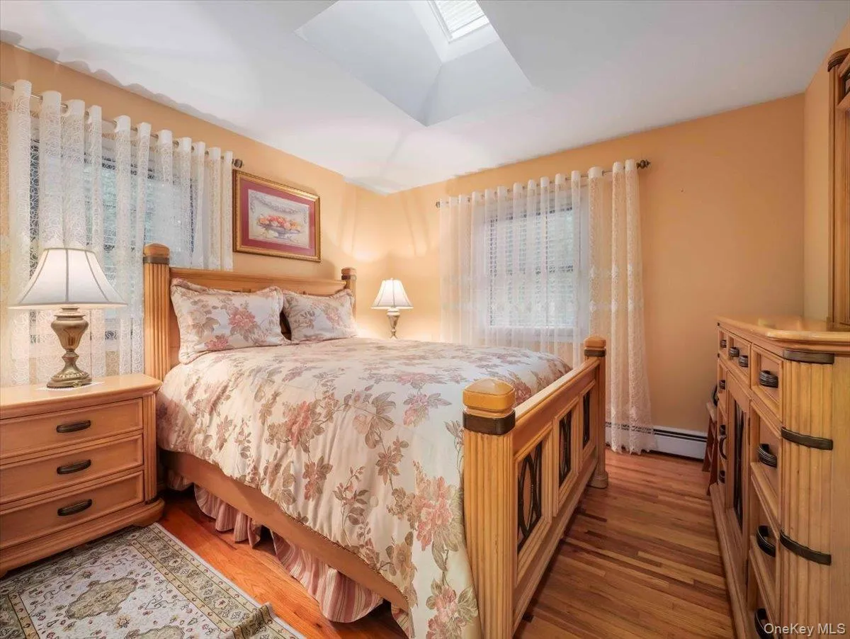 Bedroom featuring hardwood flooring, a skylight, and two windows with blinds Bedroom featuring hardwood flooring, a skylight, and two windows with blinds