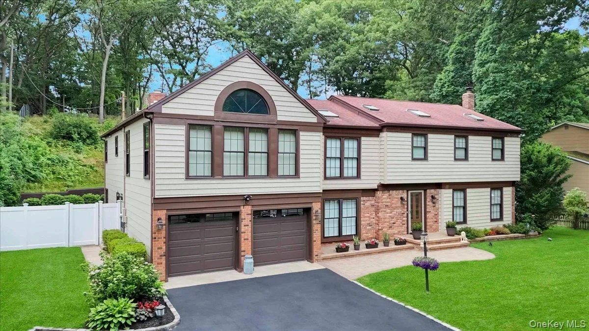 Two-story residence featuring light-toned siding with brown trim accents, a red shingle roof with skylights, and a brick facade detail Two-story residence featuring light-toned siding with brown trim accents, a red shingle roof with skylights, and a brick facade detail