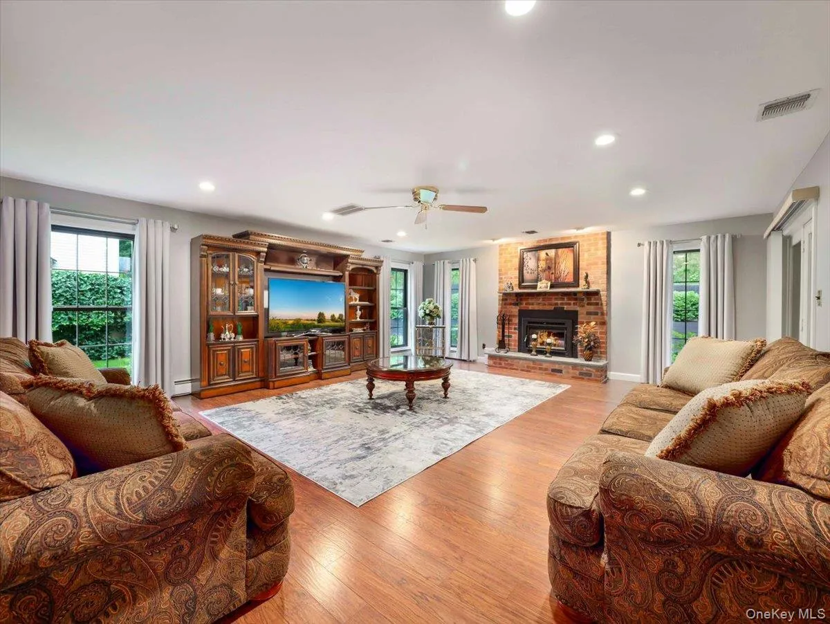 Spacious living area featuring wood-finish flooring, a prominent brick fireplace, and recessed lighting Spacious living area featuring wood-finish flooring, a prominent brick fireplace, and recessed lighting