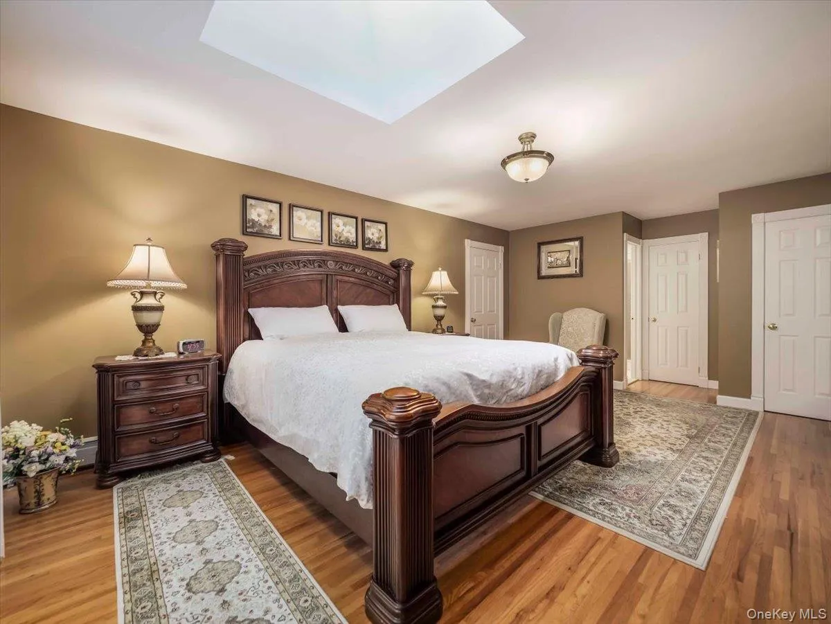 Bedroom featuring wood-finish flooring, a ceiling-mounted light fixture, and a skylight Bedroom featuring wood-finish flooring, a ceiling-mounted light fixture, and a skylight