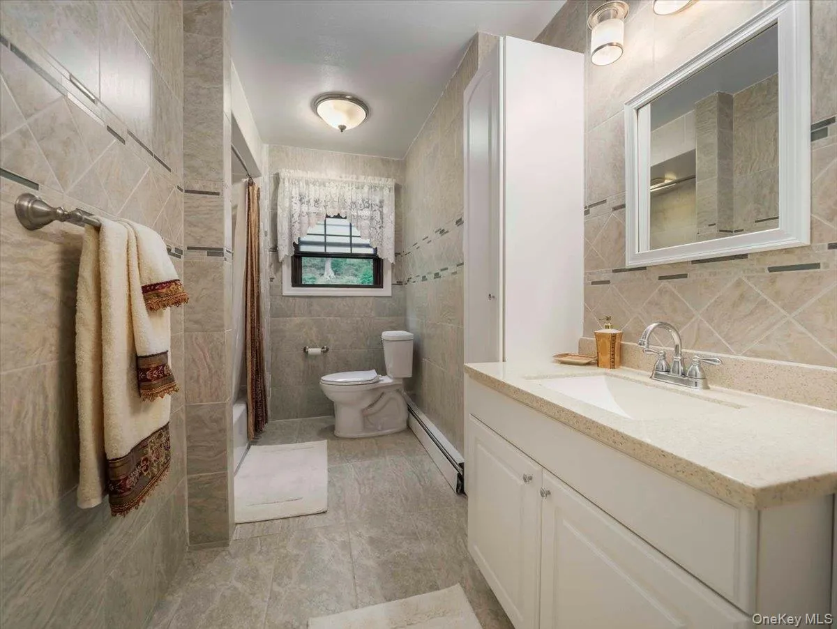 Full bathroom with a white vanity featuring a light-toned countertop, a framed mirror, and a white storage cabinet Full bathroom with a white vanity featuring a light-toned countertop, a framed mirror, and a white storage cabinet