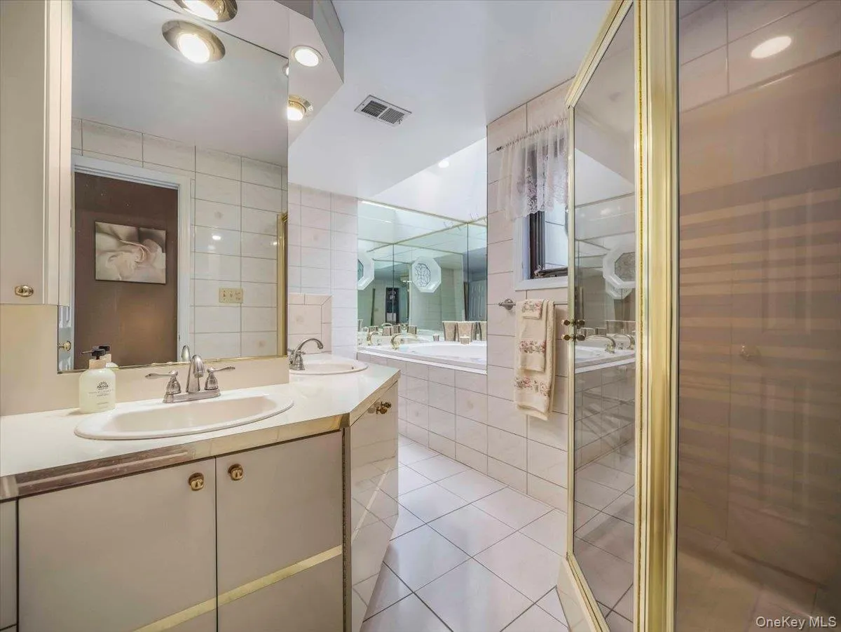 Bathroom featuring dual vanity with built-in storage, a tiled soaking tub, and a glass-enclosed shower Bathroom featuring dual vanity with built-in storage, a tiled soaking tub, and a glass-enclosed shower
