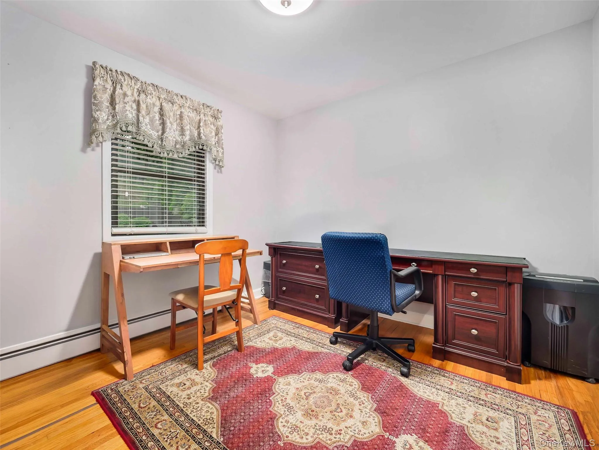 Room featuring hardwood flooring, white baseboards, and a window with blinds Room featuring hardwood flooring, white baseboards, and a window with blinds