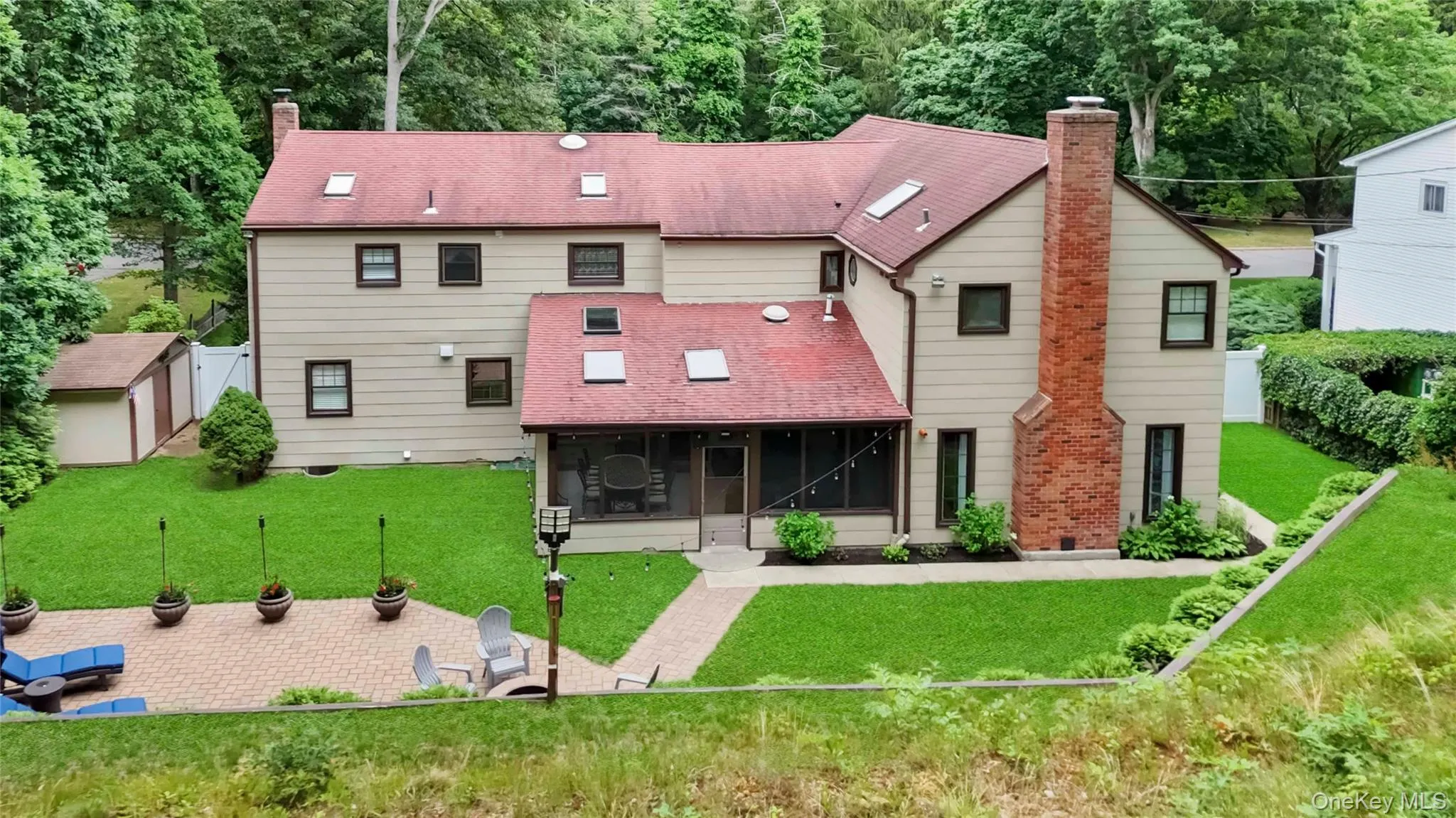 Expansive rear exterior featuring a red shingle roof with skylights, a screened porch, and a large paver patio Expansive rear exterior featuring a red shingle roof with skylights, a screened porch, and a large paver patio