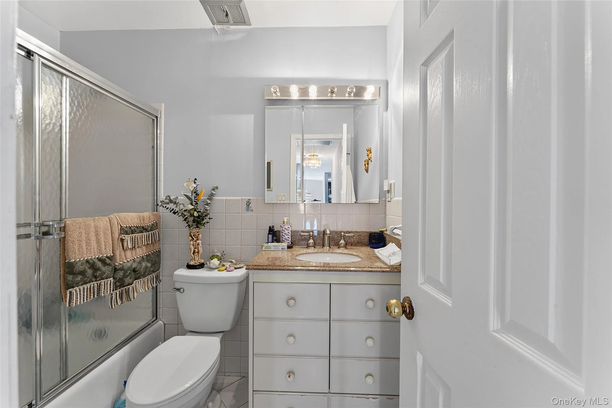 Bathroom featuring a tub/shower combination with sliding glass doors, a vanity with a light-colored countertop, and a mirrored medicine cabinet with overhead lighting Bathroom featuring a tub/shower combination with sliding glass doors, a vanity with a light-colored countertop, and a mirrored medicine cabinet with overhead lighting