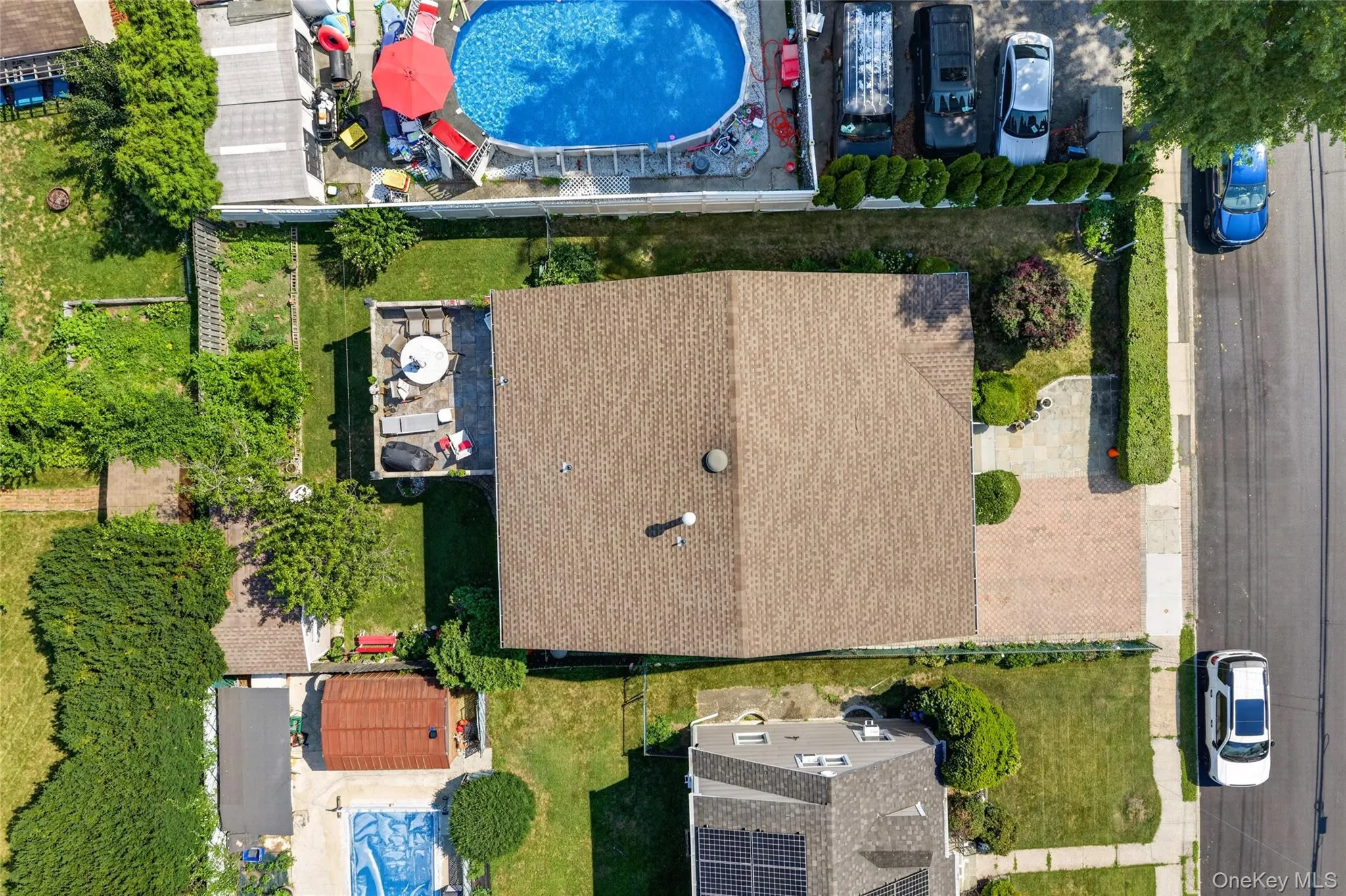 Brown shingle roof with a rear elevated patio, accompanied by a front paver driveway and mature landscaping Brown shingle roof with a rear elevated patio, accompanied by a front paver driveway and mature landscaping