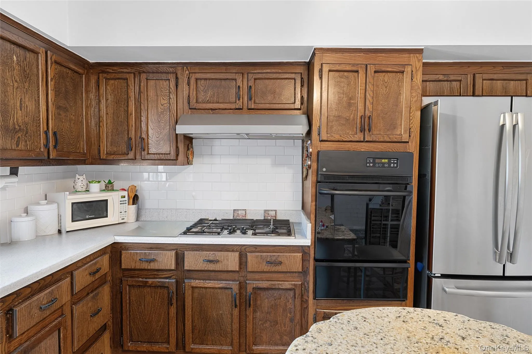 Kitchen featuring extensive wood cabinetry, white subway tile backsplash, white countertops, built-in gas range, and double wall ovens Kitchen featuring extensive wood cabinetry, white subway tile backsplash, white countertops, built-in gas range, and double wall ovens