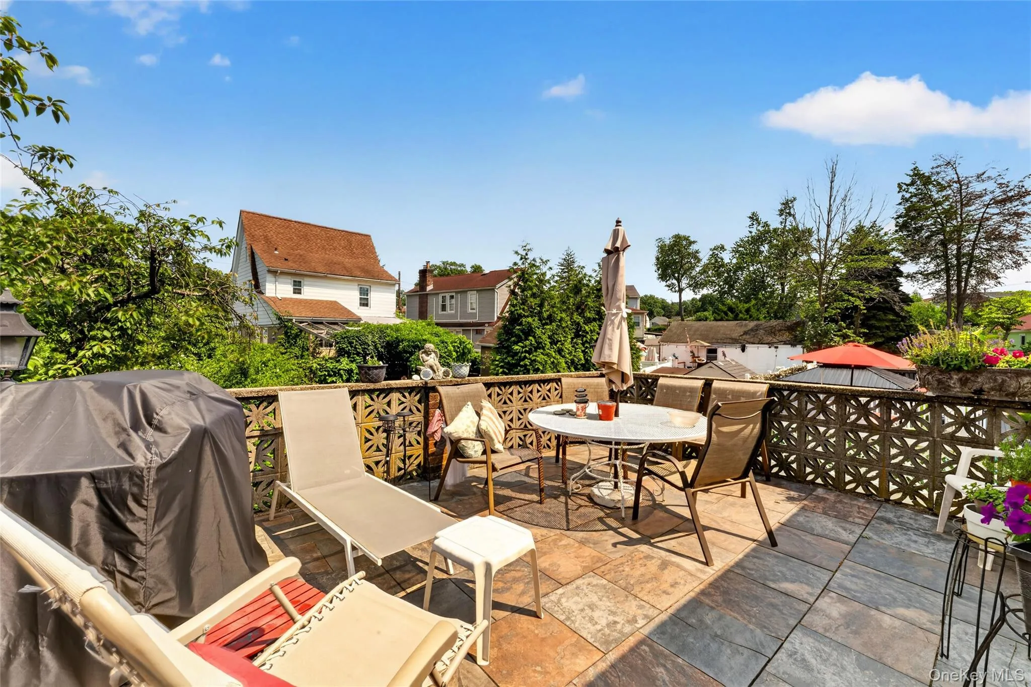 Spacious outdoor patio featuring multi-toned stone tile flooring, an openwork geometric pattern railing, and mature green foliage Spacious outdoor patio featuring multi-toned stone tile flooring, an openwork geometric pattern railing, and mature green foliage