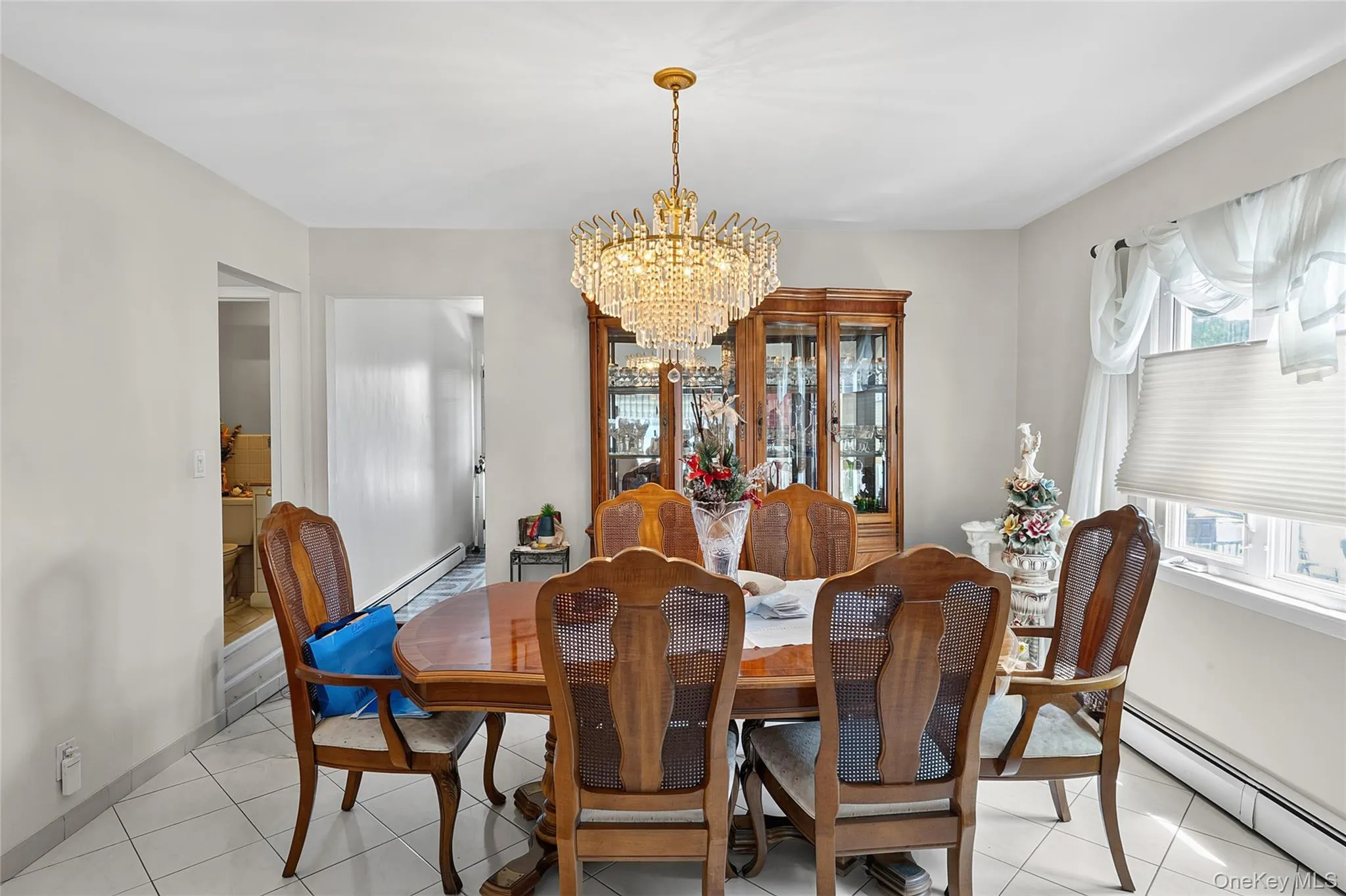 Dining area featuring a central crystal chandelier, tiled flooring, and neutral wall tones Dining area featuring a central crystal chandelier, tiled flooring, and neutral wall tones