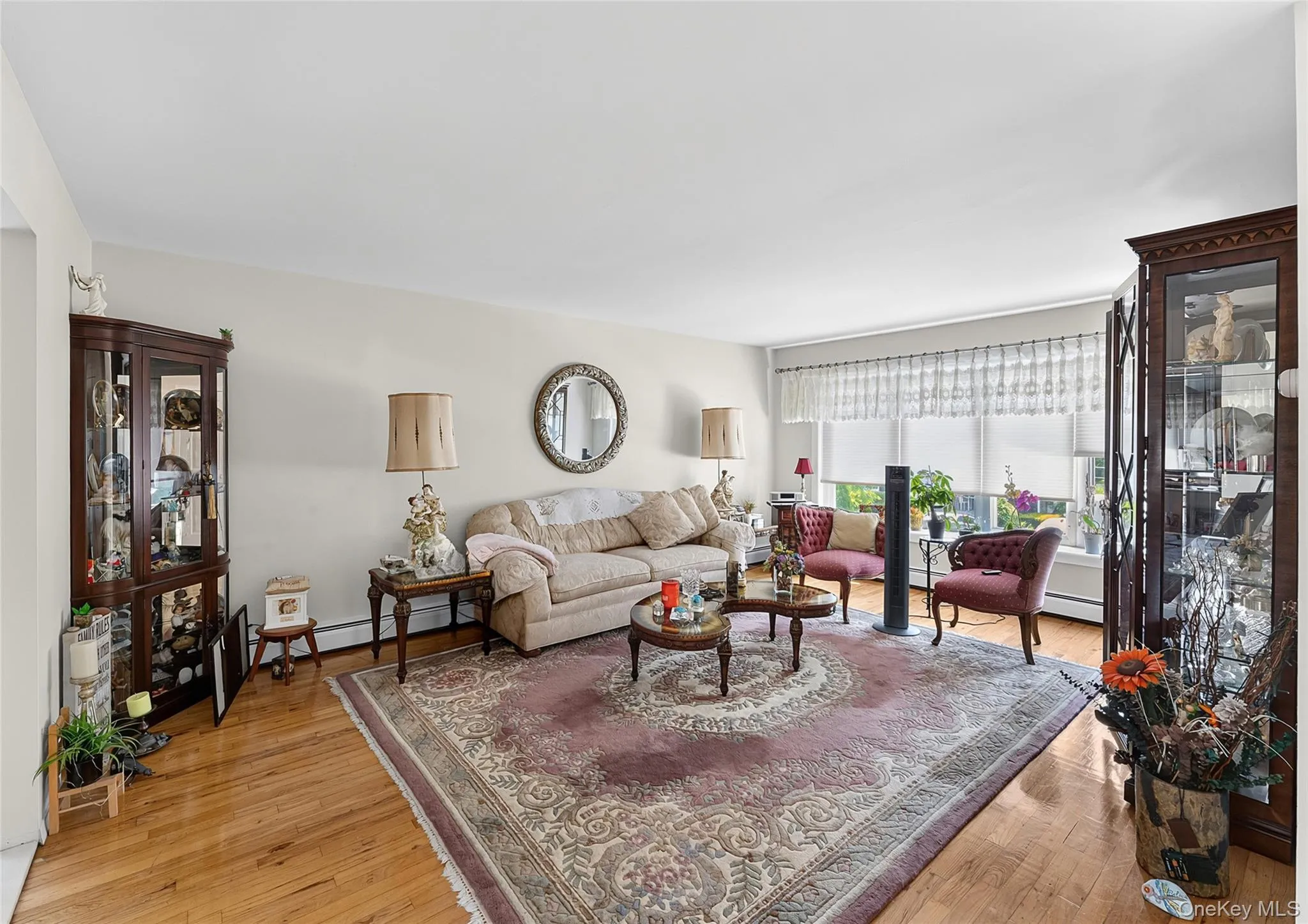 Spacious living area featuring polished wood-finish flooring, ample natural light from large windows, and neutral wall tones Spacious living area featuring polished wood-finish flooring, ample natural light from large windows, and neutral wall tones
