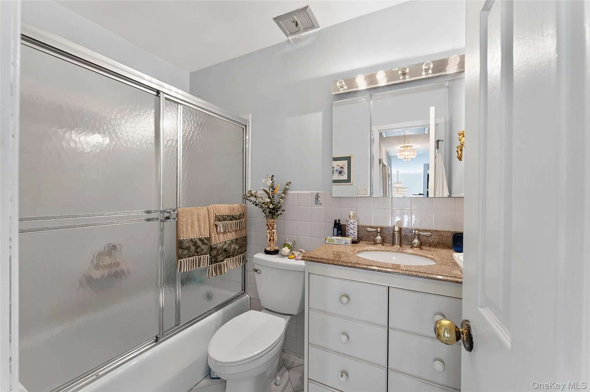 Bathroom featuring a shower/tub combination with sliding frosted glass doors, a vanity with a light-colored countertop and integrated sink, a mirrored medicine cabinet, and overhead lighting Bathroom featuring a shower/tub combination with sliding frosted glass doors, a vanity with a light-colored countertop and integrated sink, a mirrored medicine cabinet, and overhead lighting