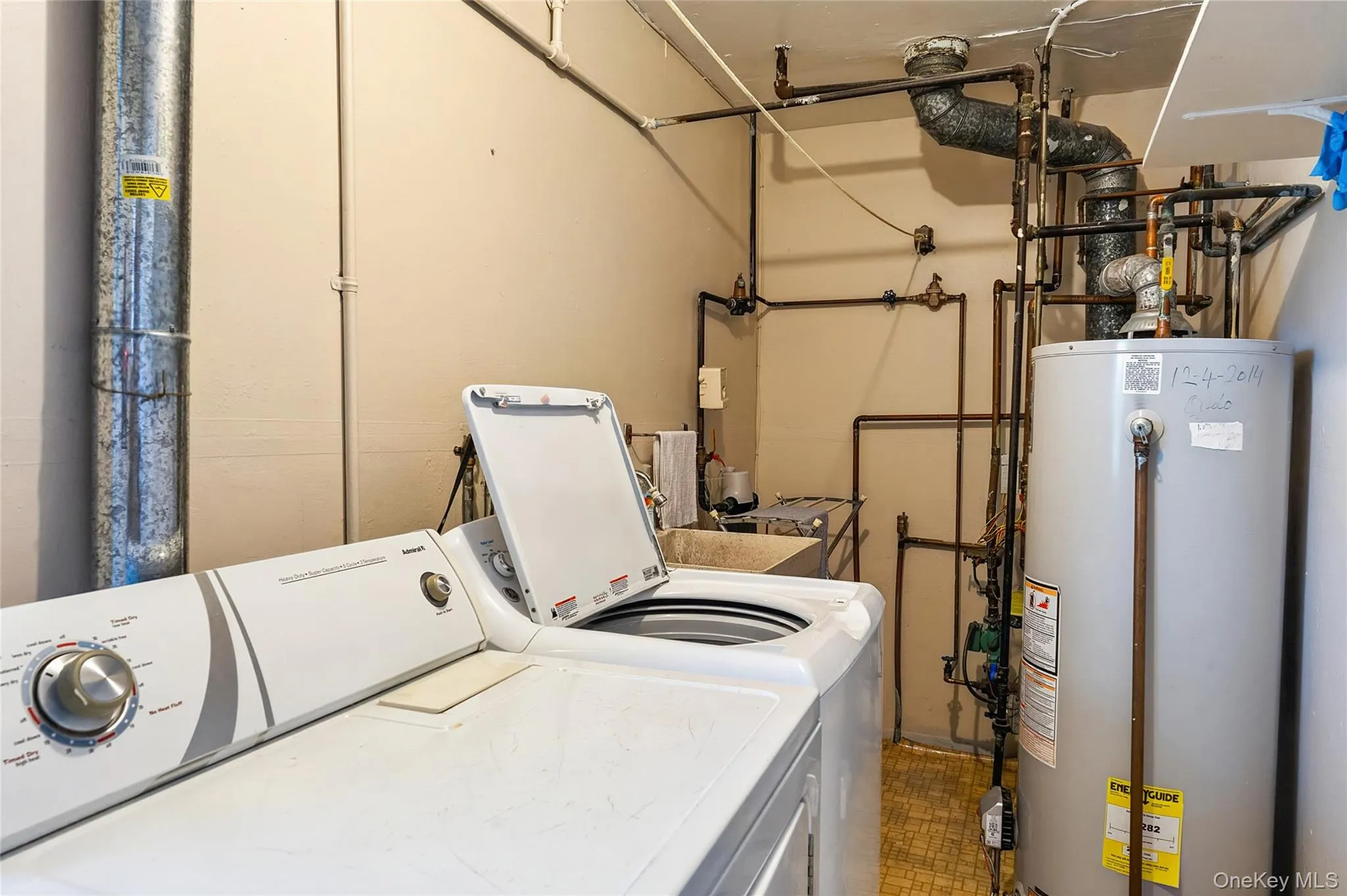 Utility area featuring a top-load washing machine, a water heater, a utility sink, exposed piping, and a large metal duct Utility area featuring a top-load washing machine, a water heater, a utility sink, exposed piping, and a large metal duct