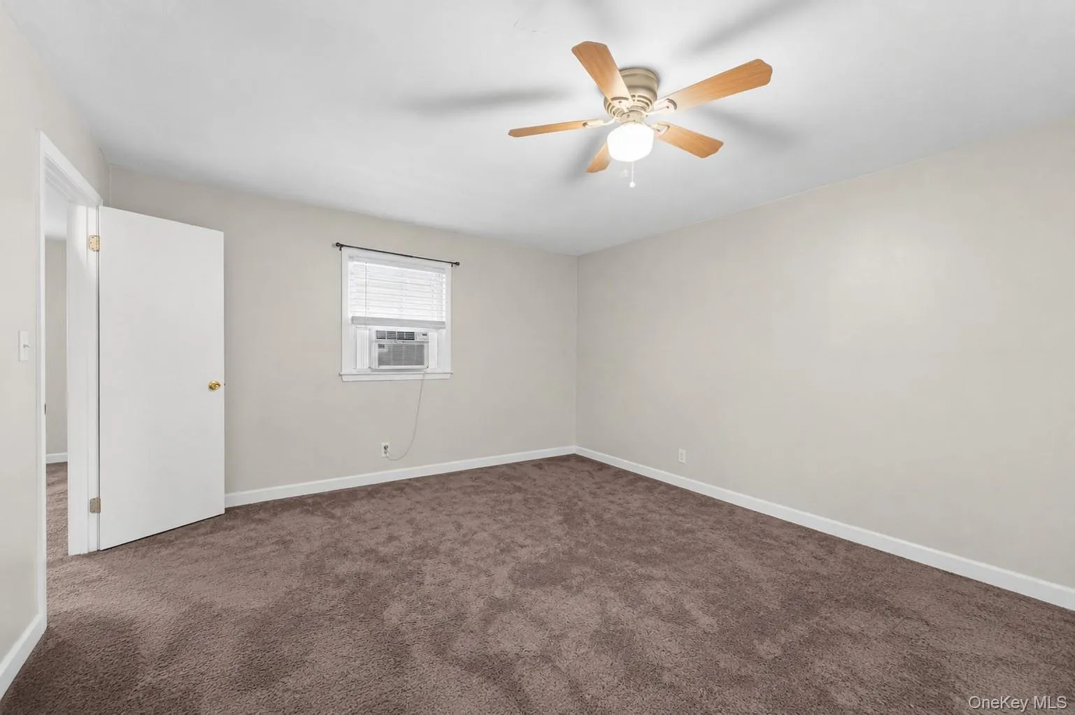 Spacious room featuring neutral wall tones, brown carpeting, a window with horizontal blinds, and a ceiling fan with light fixture Spacious room featuring neutral wall tones, brown carpeting, a window with horizontal blinds, and a ceiling fan with light fixture