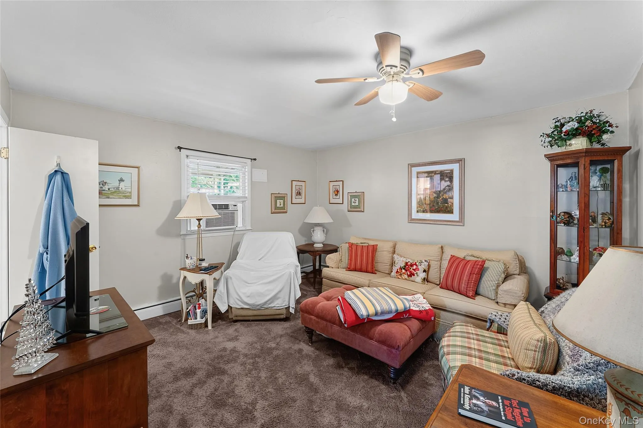 Carpeted living area featuring a ceiling fan with light fixture, window with blinds, and white painted walls Carpeted living area featuring a ceiling fan with light fixture, window with blinds, and white painted walls