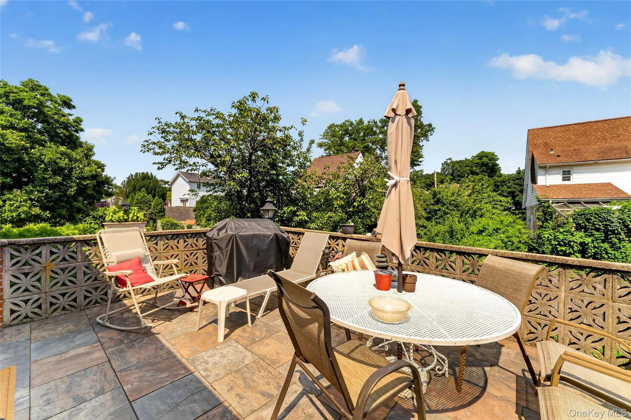 Expansive outdoor patio featuring flagstone flooring, a decorative block privacy wall, and mature perimeter trees Expansive outdoor patio featuring flagstone flooring, a decorative block privacy wall, and mature perimeter trees