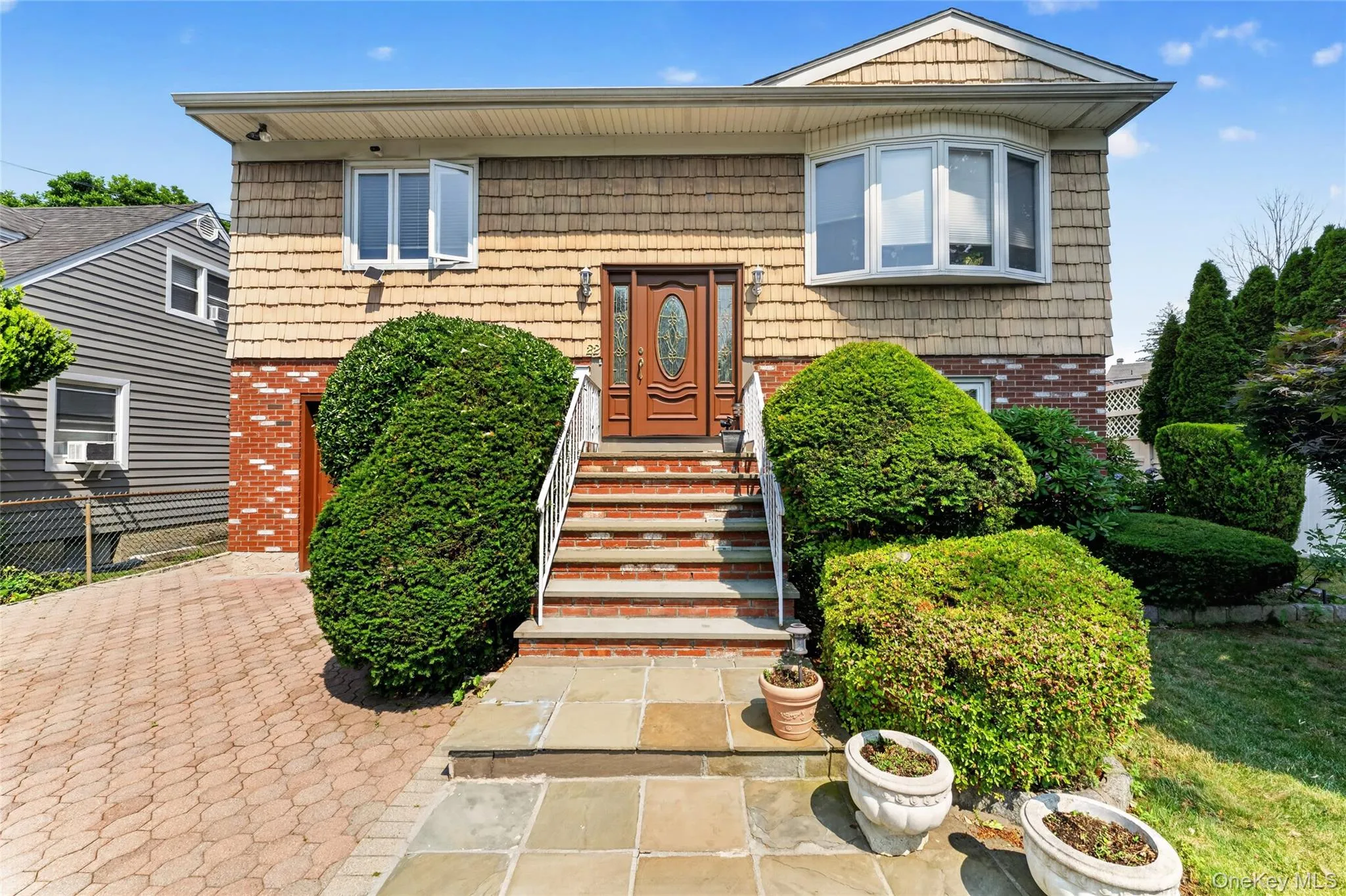 Front elevation featuring shake siding, brick accents, a wood-finish entry door, a bay window, and a paver driveway Front elevation featuring shake siding, brick accents, a wood-finish entry door, a bay window, and a paver driveway