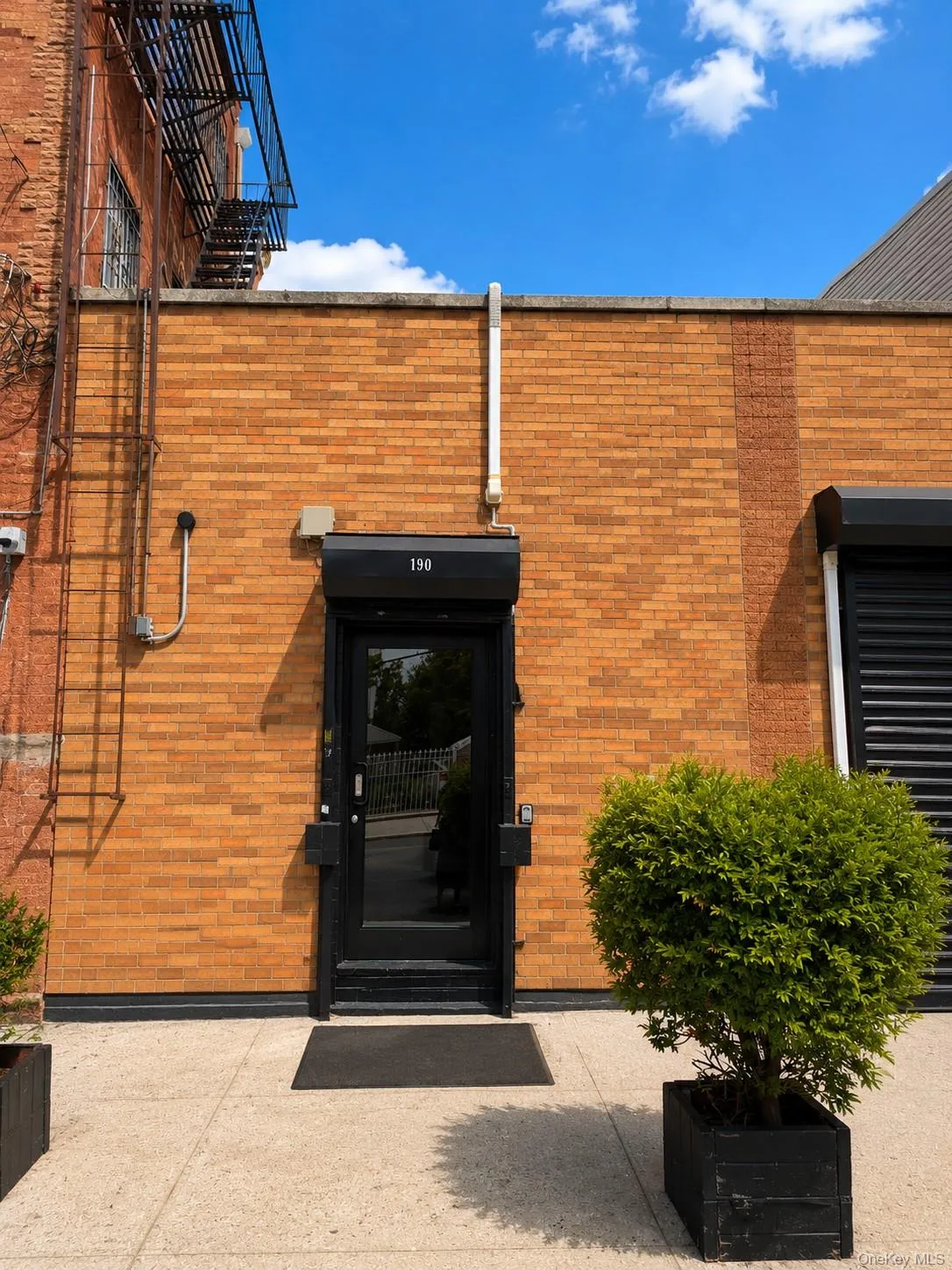 Brick exterior featuring a black entry door with transom window, concrete walkway, and decorative planter Brick exterior featuring a black entry door with transom window, concrete walkway, and decorative planter