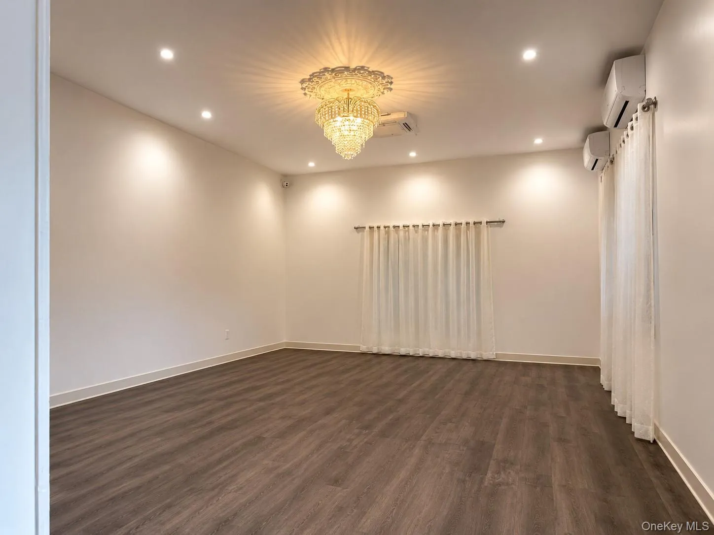 Spacious room featuring wood-finish flooring, recessed lighting, and a prominent crystal chandelier Spacious room featuring wood-finish flooring, recessed lighting, and a prominent crystal chandelier