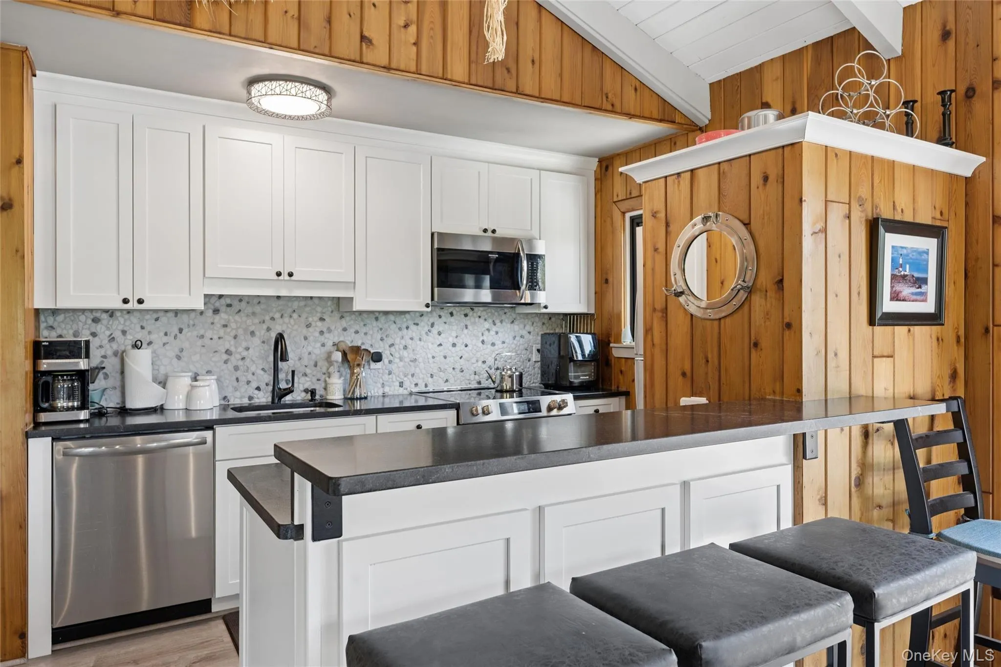 Kitchen featuring white shaker-style cabinetry, a gray mosaic tile backsplash, black countertops, and stainless steel appliances Kitchen featuring white shaker-style cabinetry, a gray mosaic tile backsplash, black countertops, and stainless steel appliances