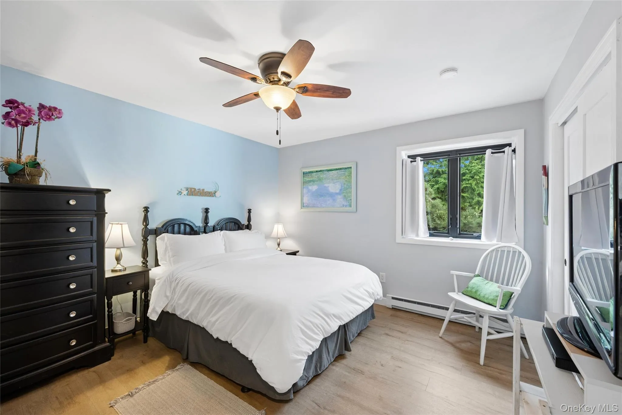 Bedroom featuring wood-finish flooring, a ceiling fan with light fixture, and a window with exterior tree scenery Bedroom featuring wood-finish flooring, a ceiling fan with light fixture, and a window with exterior tree scenery