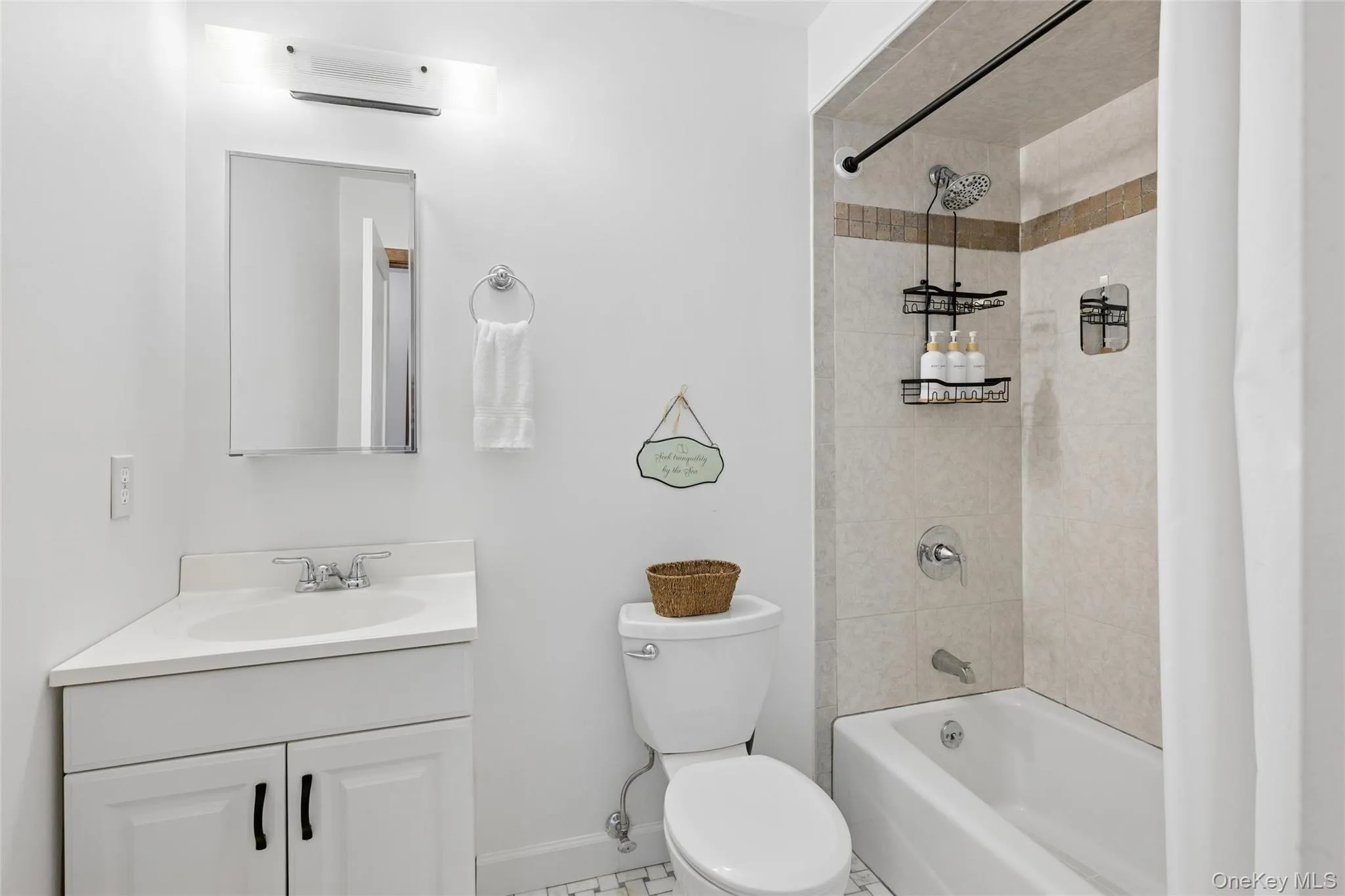 Bathroom featuring a white vanity with integrated sink, coordinating white toilet, and a tiled shower/tub combination with a decorative accent band Bathroom featuring a white vanity with integrated sink, coordinating white toilet, and a tiled shower/tub combination with a decorative accent band