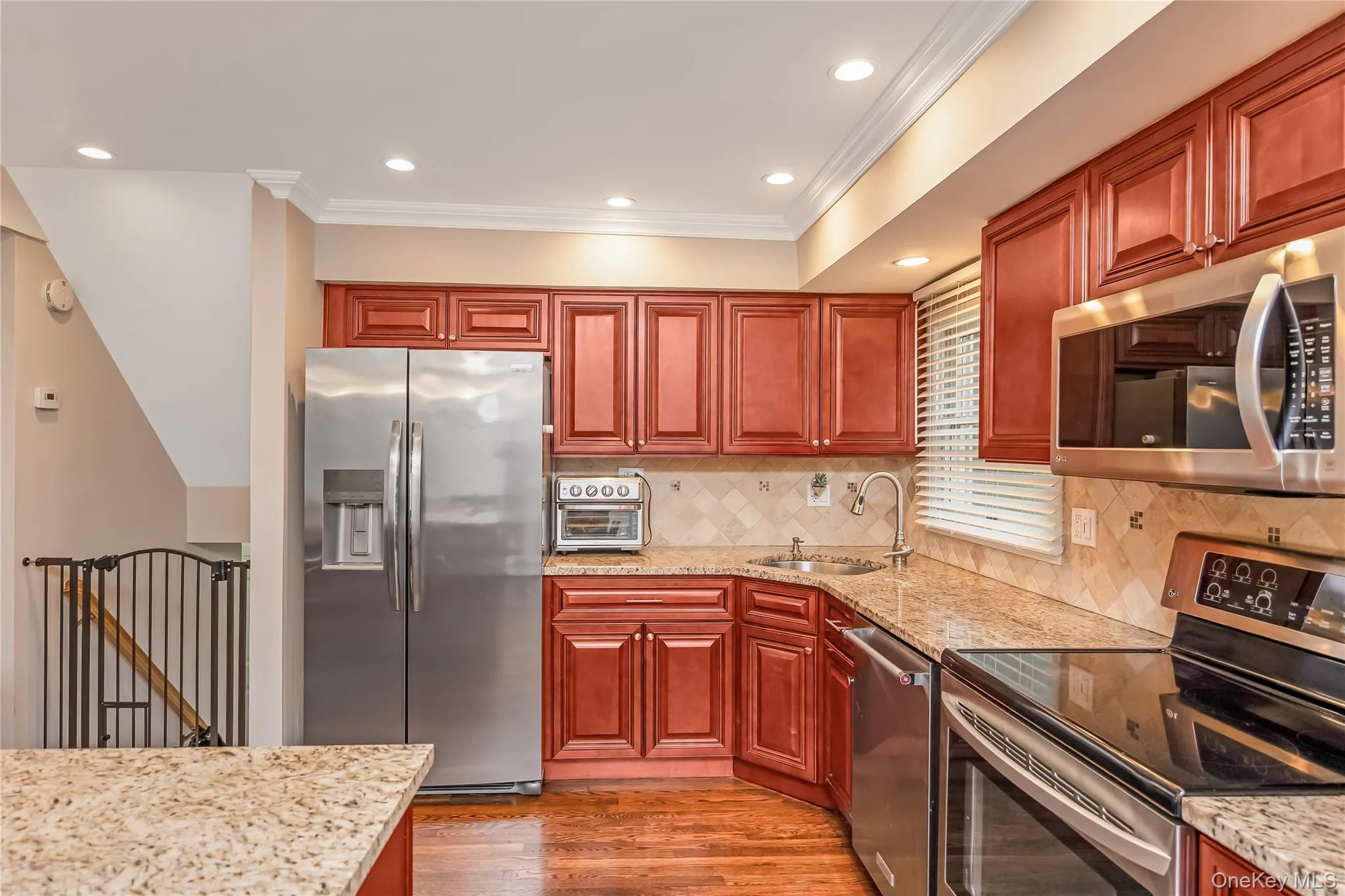 Kitchen featuring wood-finish cabinetry, stainless steel appliances, granite-style countertops, and a tile backsplash Kitchen featuring wood-finish cabinetry, stainless steel appliances, granite-style countertops, and a tile backsplash
