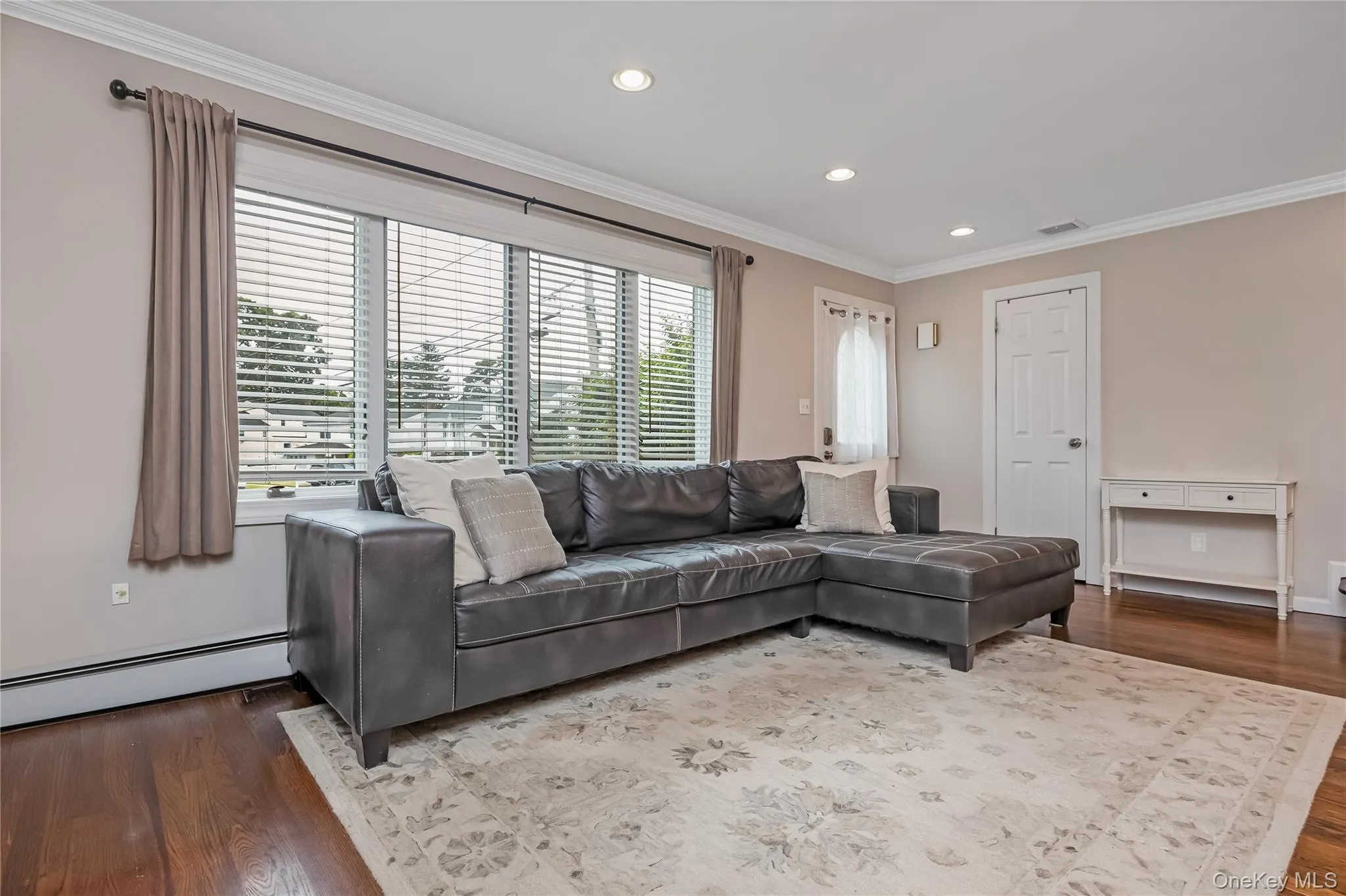 Living area featuring expansive windows with horizontal blinds, rich wood-finish flooring, recessed lighting, and crown molding Living area featuring expansive windows with horizontal blinds, rich wood-finish flooring, recessed lighting, and crown molding
