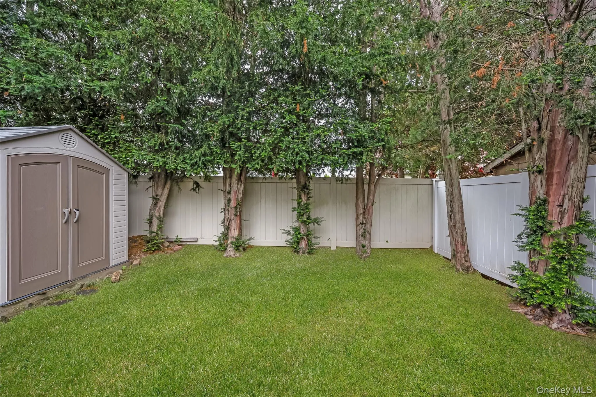 Yard featuring a storage shed, mature trees, and a white privacy fence Yard featuring a storage shed, mature trees, and a white privacy fence