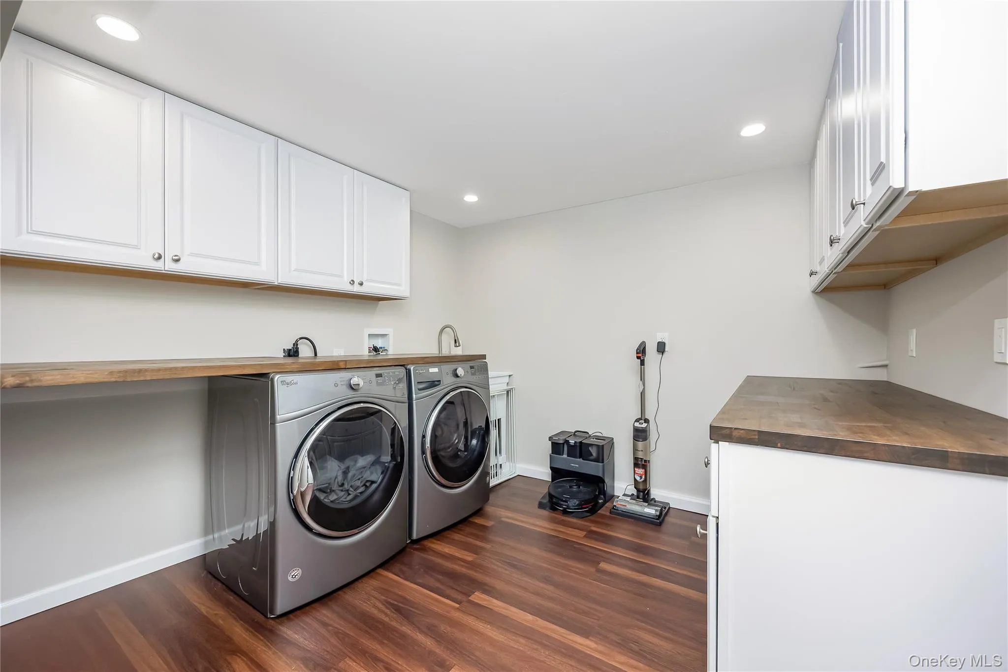 Laundry room featuring wood-finish flooring, white shaker cabinetry, and wood countertops Laundry room featuring wood-finish flooring, white shaker cabinetry, and wood countertops