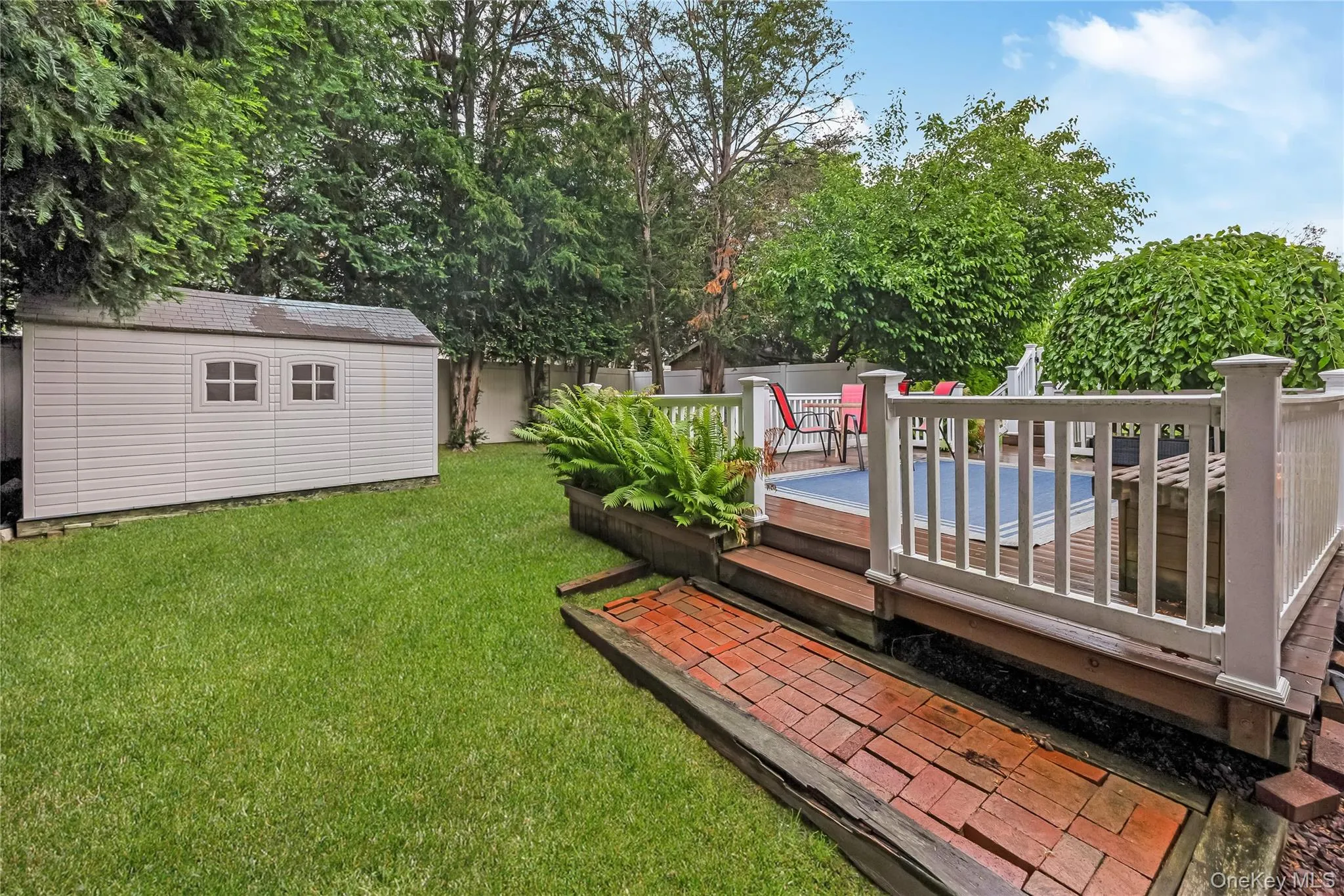 Expansive wood-finish deck with white railings, featuring direct access to interior spaces via a sliding glass door and the yard. Storage shed Expansive wood-finish deck with white railings, featuring direct access to interior spaces via a sliding glass door and the yard. Storage shed