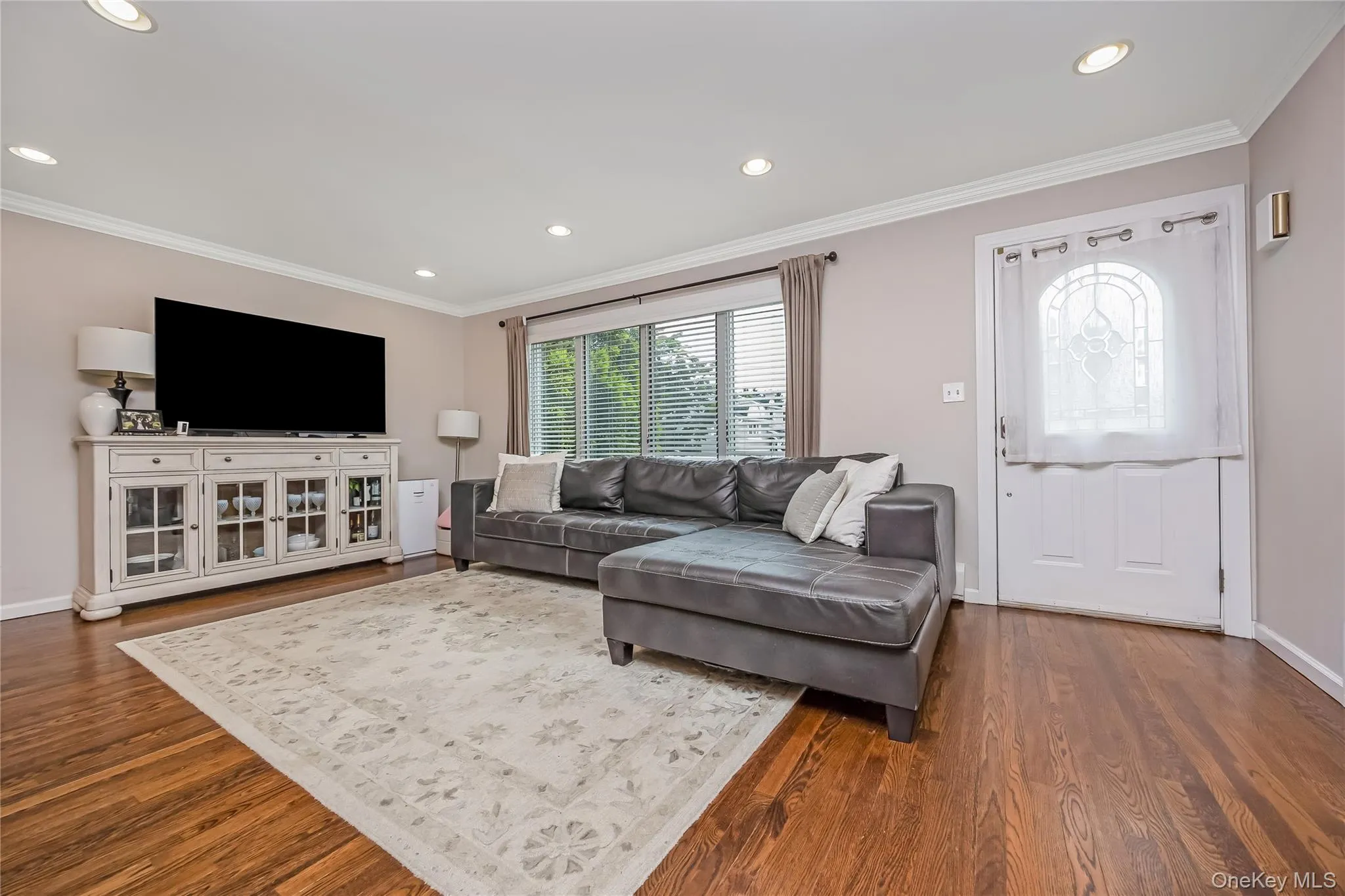 Living area featuring expansive windows with horizontal blinds, rich wood-finish flooring, recessed lighting, and crown molding Living area featuring expansive windows with horizontal blinds, rich wood-finish flooring, recessed lighting, and crown molding