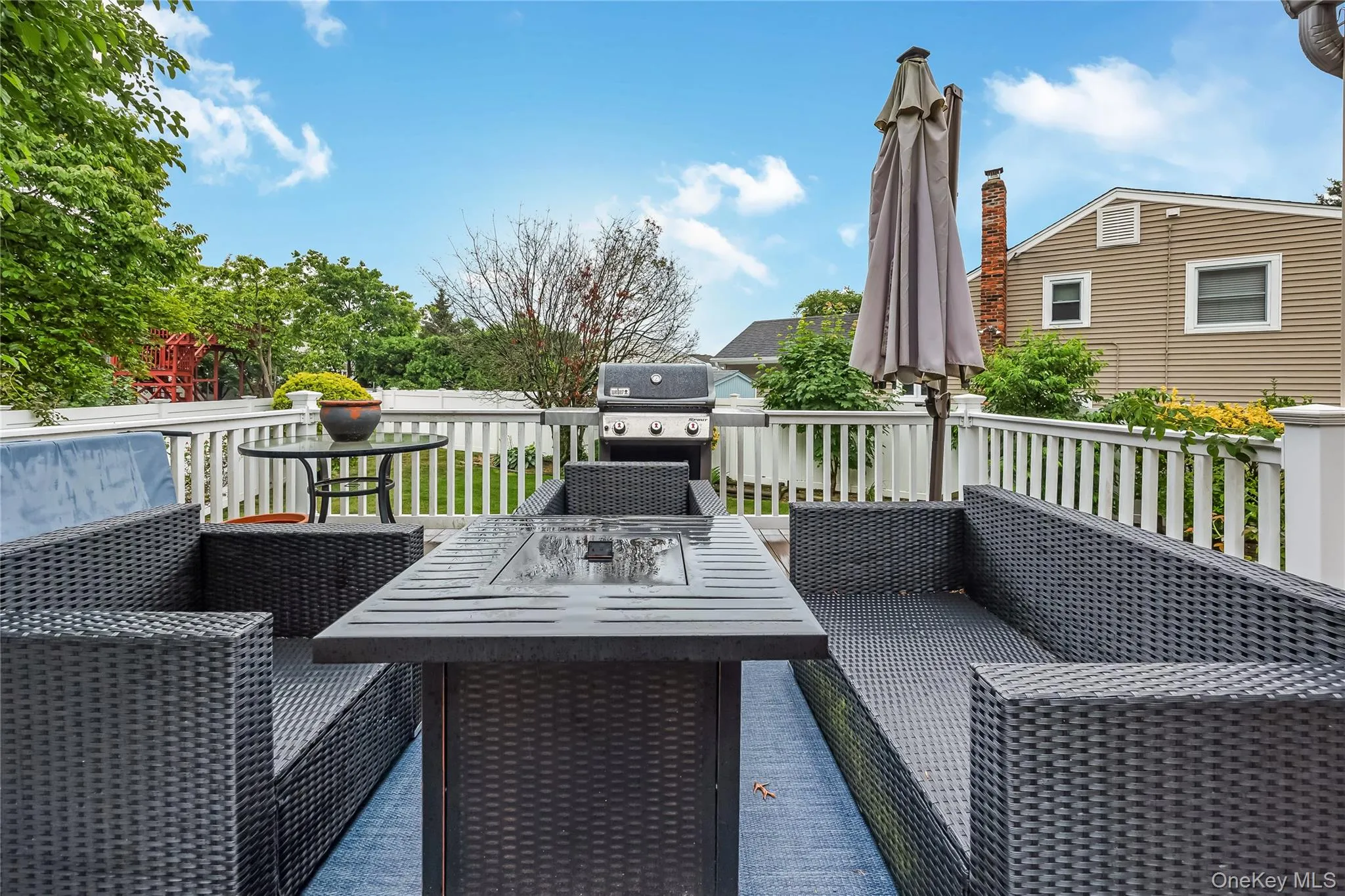 Expansive wood-finish deck with white railings, featuring direct access to interior spaces via a sliding glass door and the yard Expansive wood-finish deck with white railings, featuring direct access to interior spaces via a sliding glass door and the yard