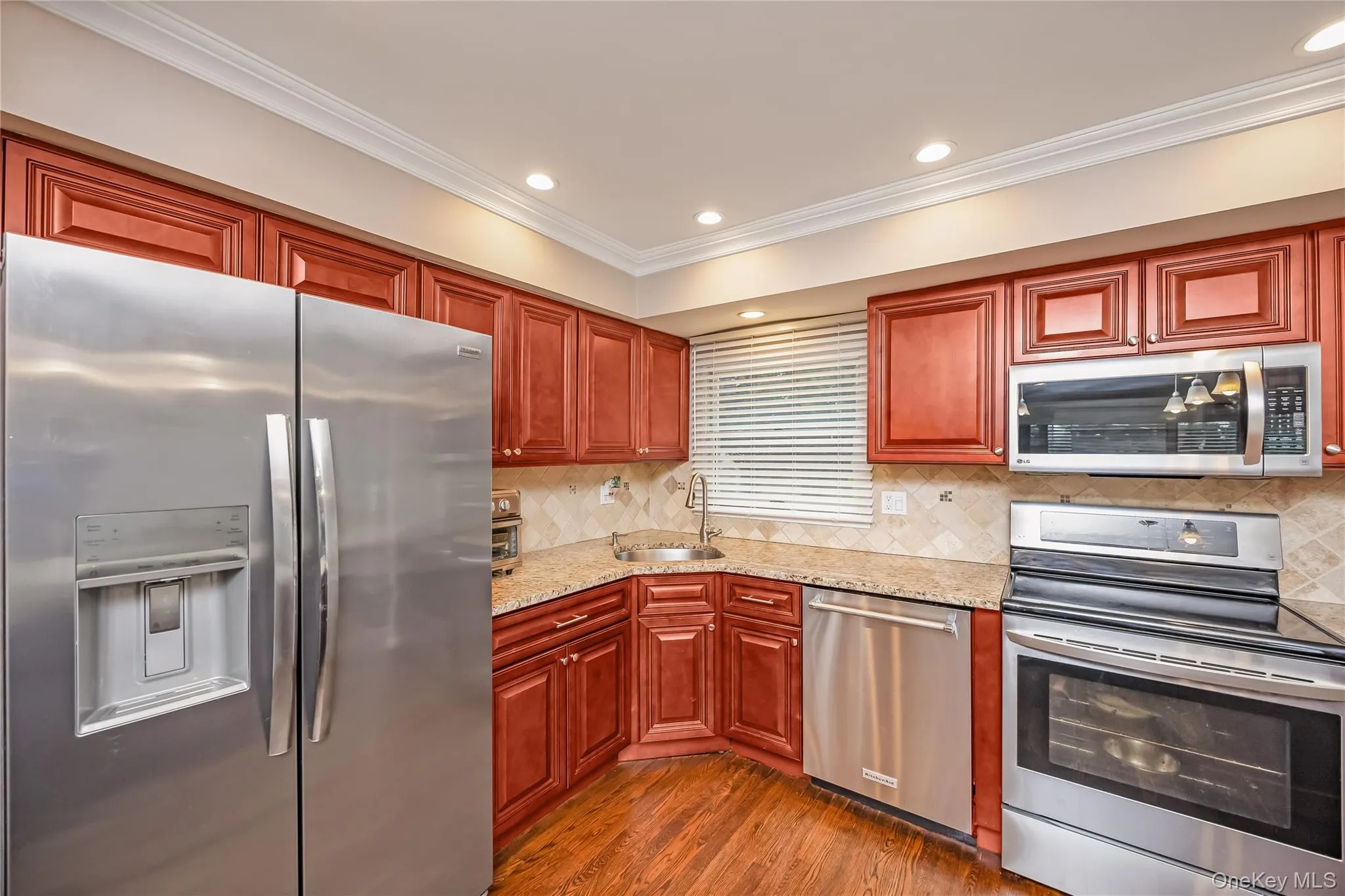 Kitchen featuring wood-finish cabinetry, stainless steel appliances, granite-style countertops, and a tile backsplash Kitchen featuring wood-finish cabinetry, stainless steel appliances, granite-style countertops, and a tile backsplash