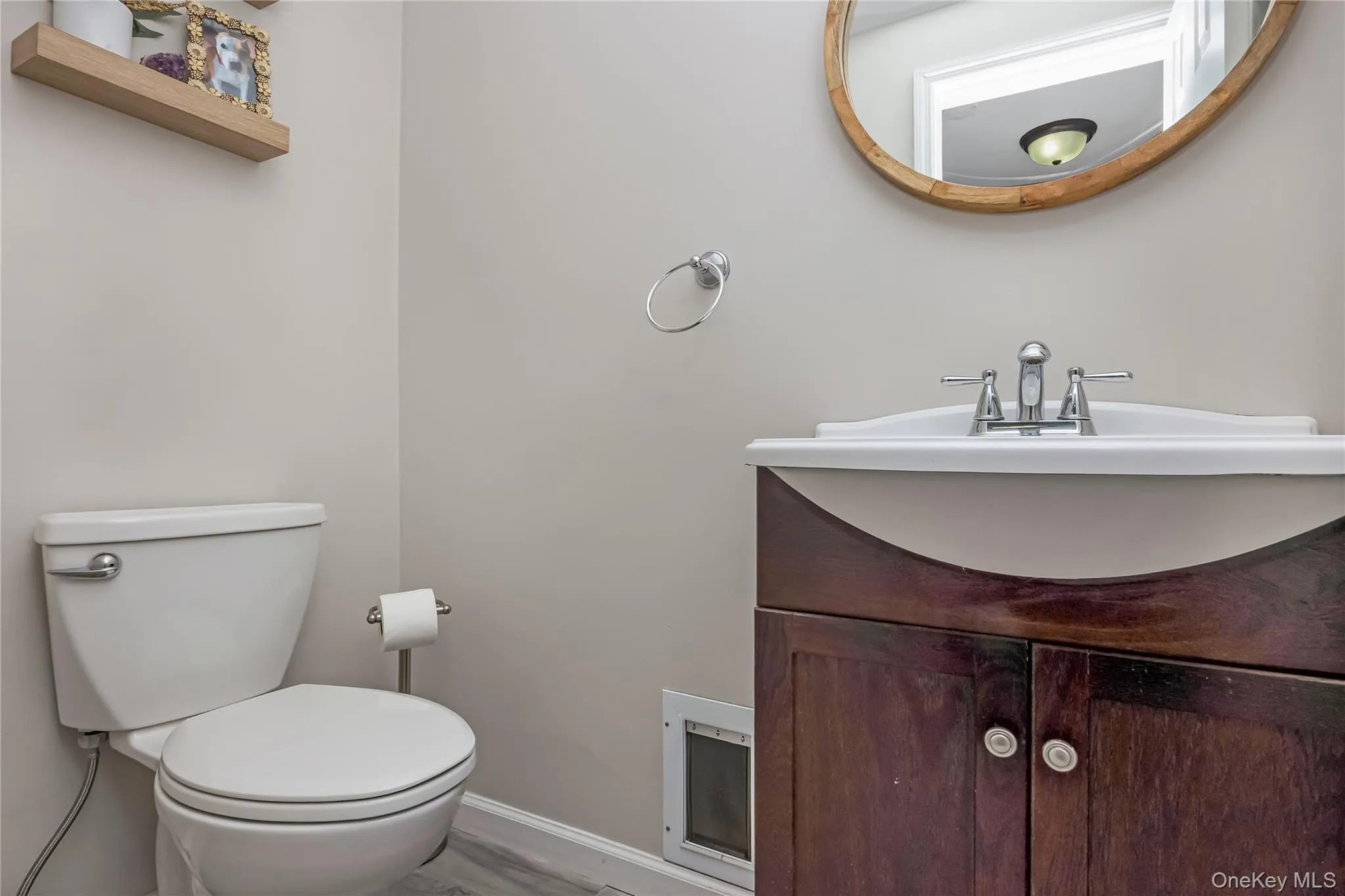 Bathroom featuring a single vanity with a dark wood-finish cabinet and white countertop, chrome faucet, and a round wood-framed mirror Bathroom featuring a single vanity with a dark wood-finish cabinet and white countertop, chrome faucet, and a round wood-framed mirror