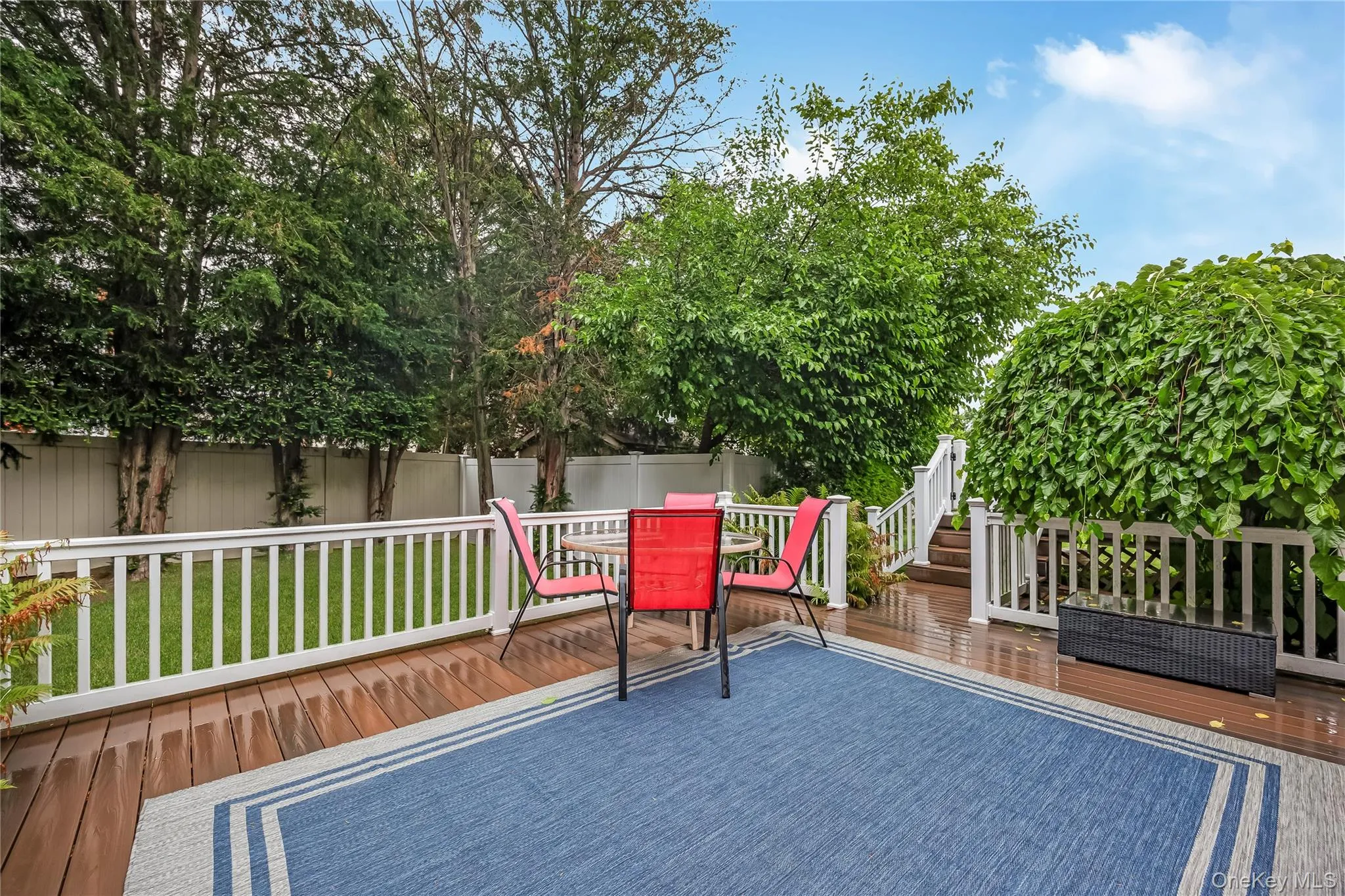 Expansive wood-finish deck with white railings, featuring direct access to interior spaces via a sliding glass door and the yard Expansive wood-finish deck with white railings, featuring direct access to interior spaces via a sliding glass door and the yard