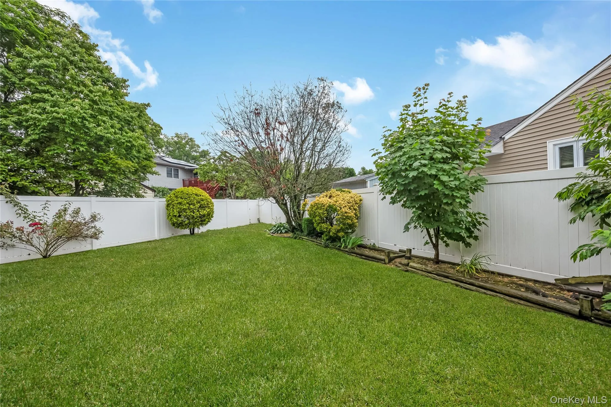 Yard featuring mature trees, and a white privacy fence Yard featuring mature trees, and a white privacy fence