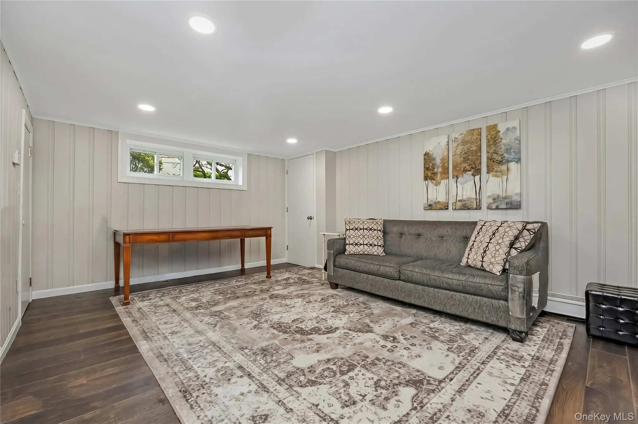 Spacious room featuring wood-finish flooring, light vertical paneling on walls, recessed ceiling lights, and multiple windows. Mechanicals and storage Spacious room featuring wood-finish flooring, light vertical paneling on walls, recessed ceiling lights, and multiple windows. Mechanicals and storage