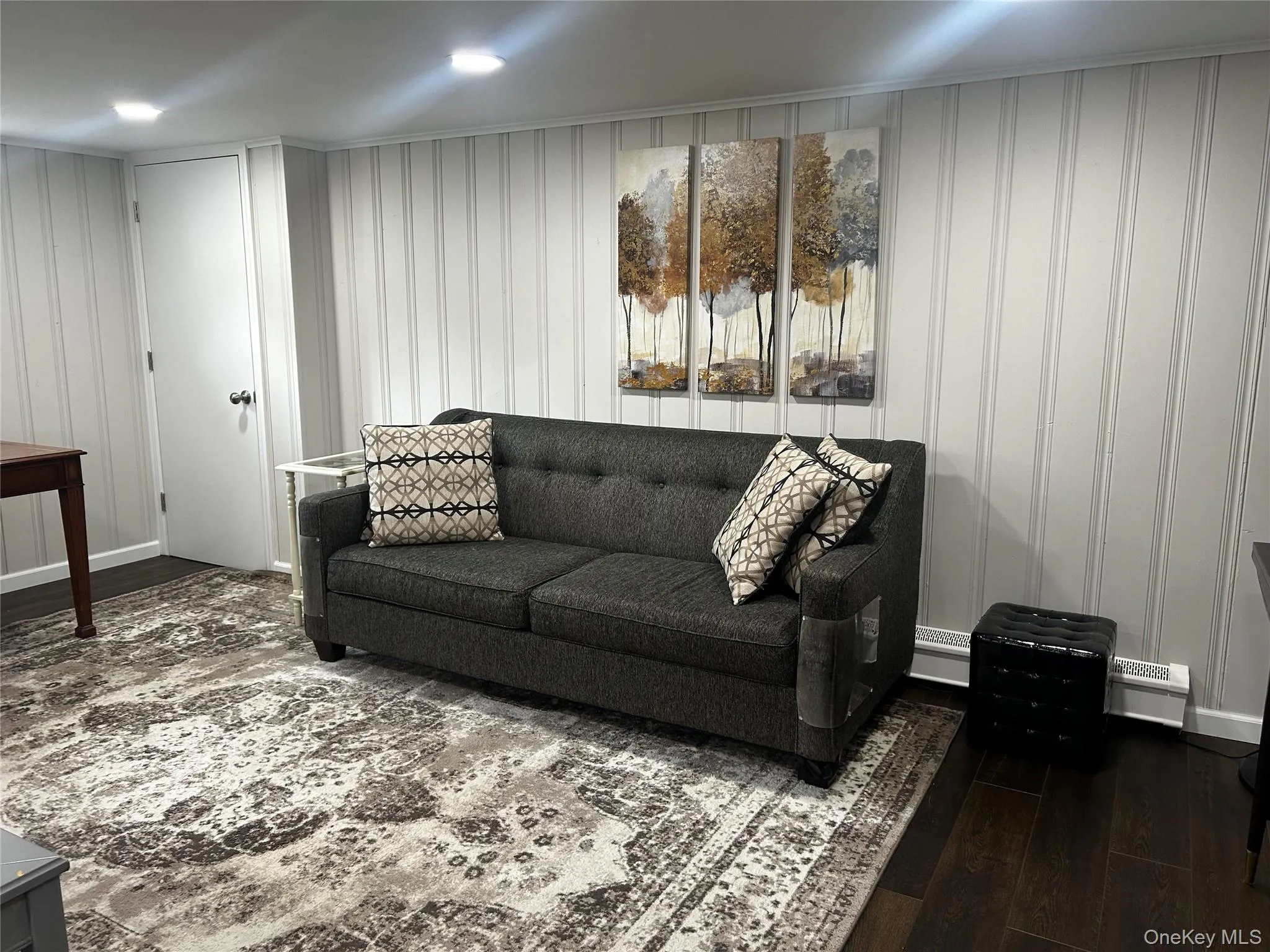 Spacious room featuring wood-finish flooring, light vertical paneling on walls, recessed ceiling lights, and multiple windows. Mechanicals and storage Spacious room featuring wood-finish flooring, light vertical paneling on walls, recessed ceiling lights, and multiple windows. Mechanicals and storage