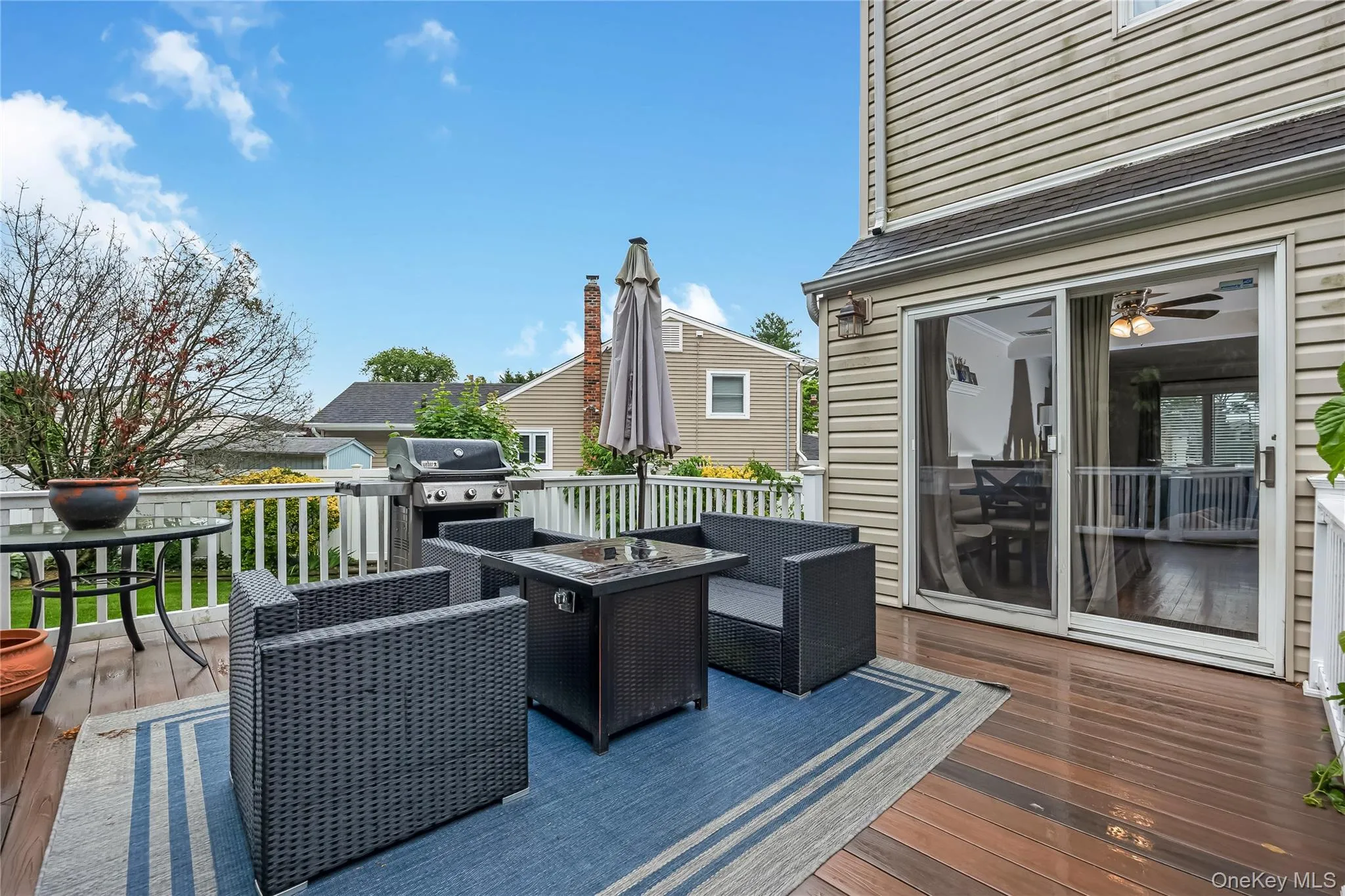 Expansive wood-finish deck with white railings, featuring direct access to interior spaces via a sliding glass door and the yard Expansive wood-finish deck with white railings, featuring direct access to interior spaces via a sliding glass door and the yard