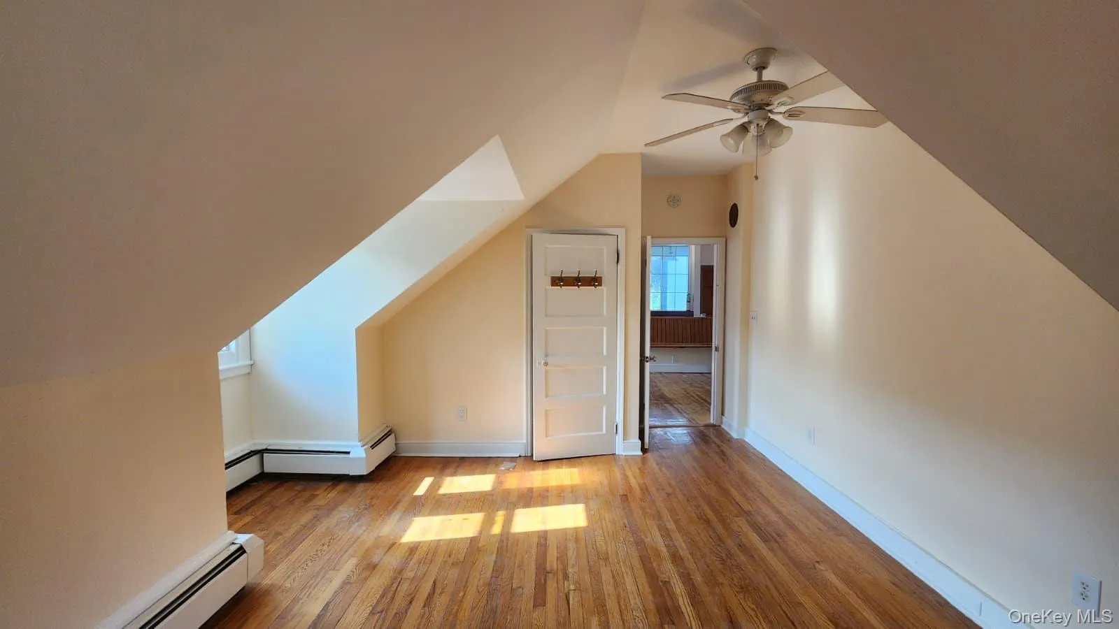 Spacious room featuring wood-finish flooring, a ceiling fan, and sloped high ceilings Spacious room featuring wood-finish flooring, a ceiling fan, and sloped high ceilings