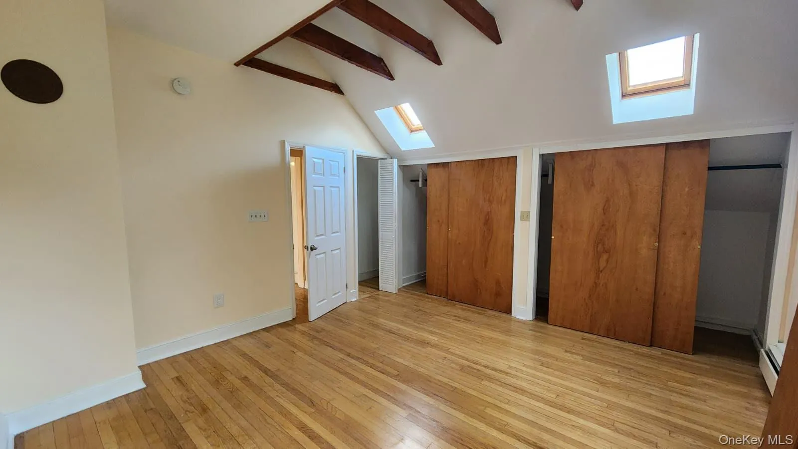 Hardwood flooring throughout this room featuring exposed wood beams, skylights, and double sliding panel closets Hardwood flooring throughout this room featuring exposed wood beams, skylights, and double sliding panel closets
