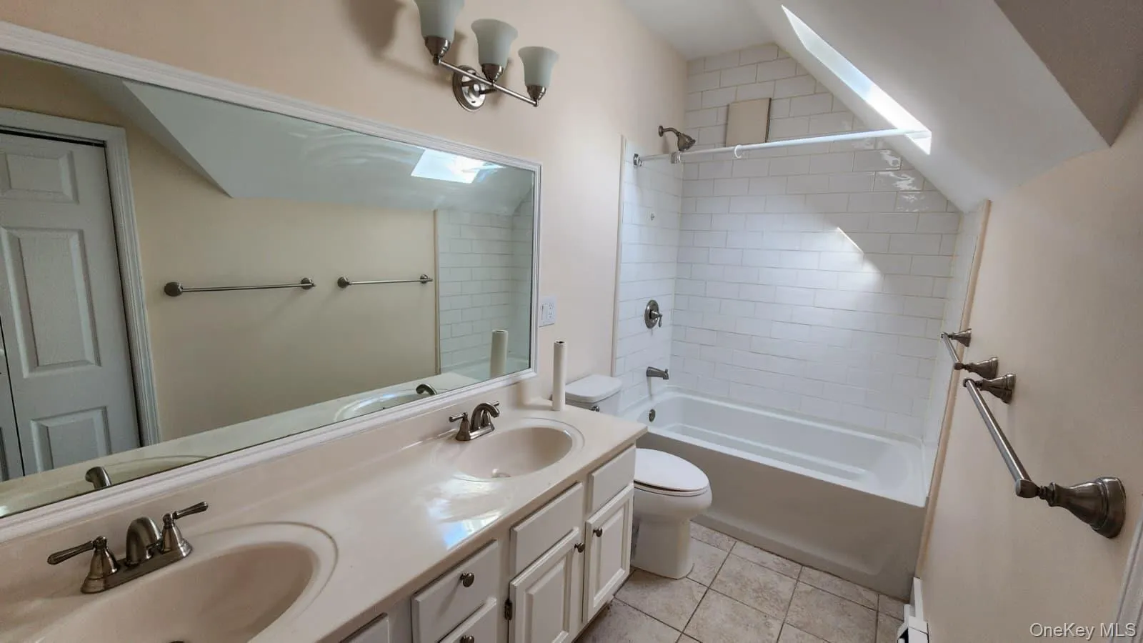 Bathroom featuring a dual vanity with integrated sinks, a built-in tub with subway tile surround, a skylight, and chrome fixtures Bathroom featuring a dual vanity with integrated sinks, a built-in tub with subway tile surround, a skylight, and chrome fixtures