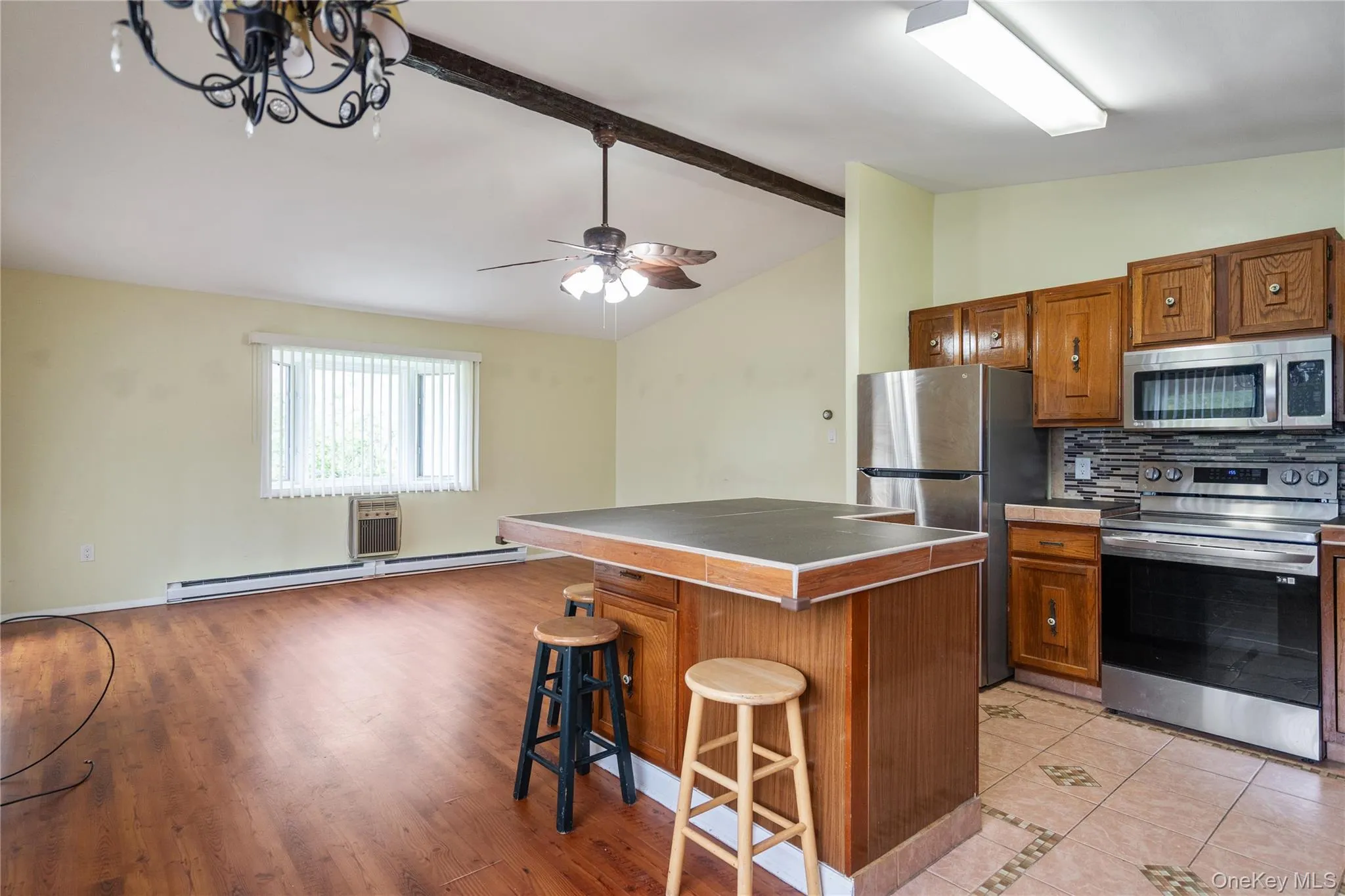 Kitchen featuring stainless steel appliances, baseboard heating, a kitchen breakfast bar, and brown cabinets Kitchen featuring stainless steel appliances, baseboard heating, a kitchen breakfast bar, and brown cabinets