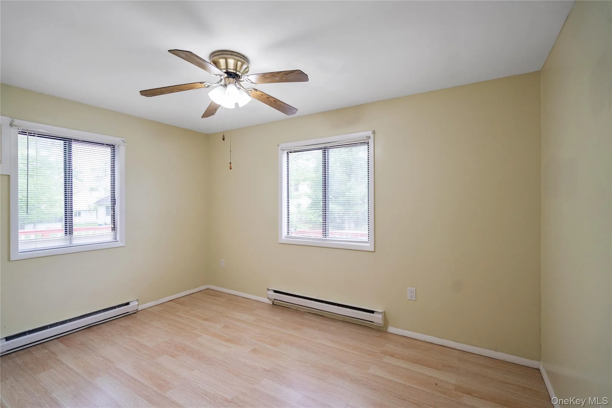 Unfurnished room featuring baseboard heating, light wood finished floors, and baseboards Unfurnished room featuring baseboard heating, light wood finished floors, and baseboards