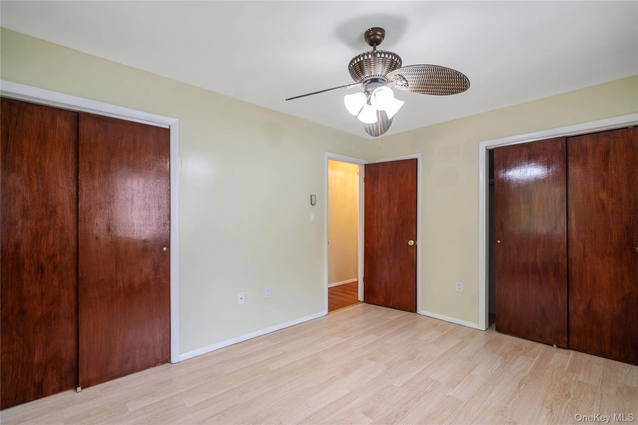 Unfurnished bedroom featuring wood finished floors, two closets, baseboards, and a ceiling fan Unfurnished bedroom featuring wood finished floors, two closets, baseboards, and a ceiling fan