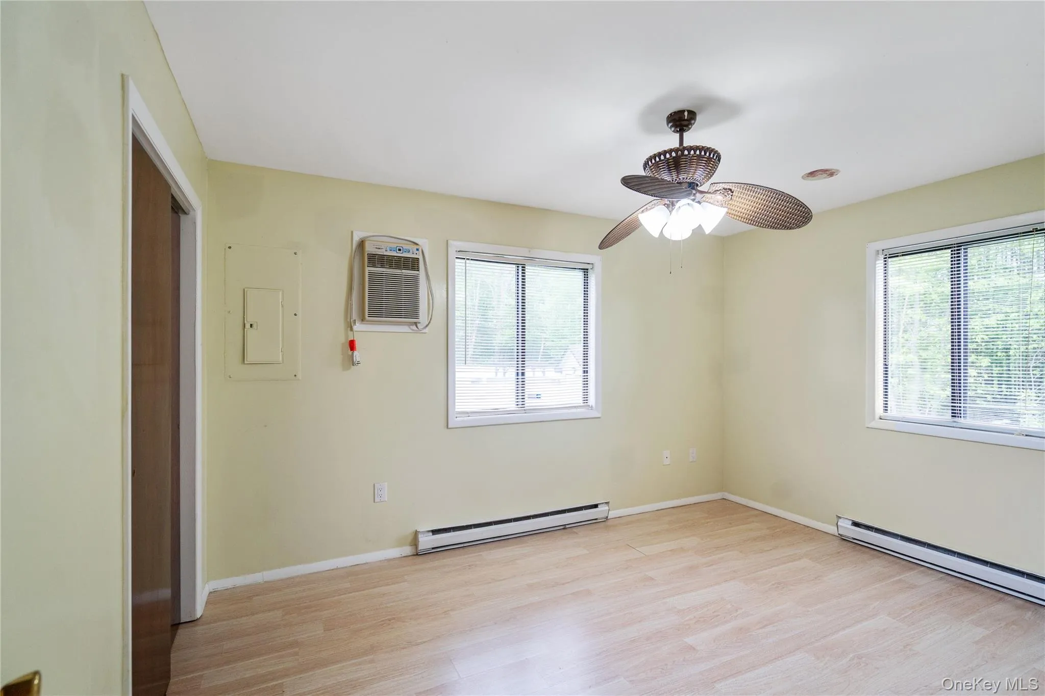 Spare room featuring baseboard heating, light wood-type flooring, a wall mounted AC, ceiling fan, and baseboards Spare room featuring baseboard heating, light wood-type flooring, a wall mounted AC, ceiling fan, and baseboards
