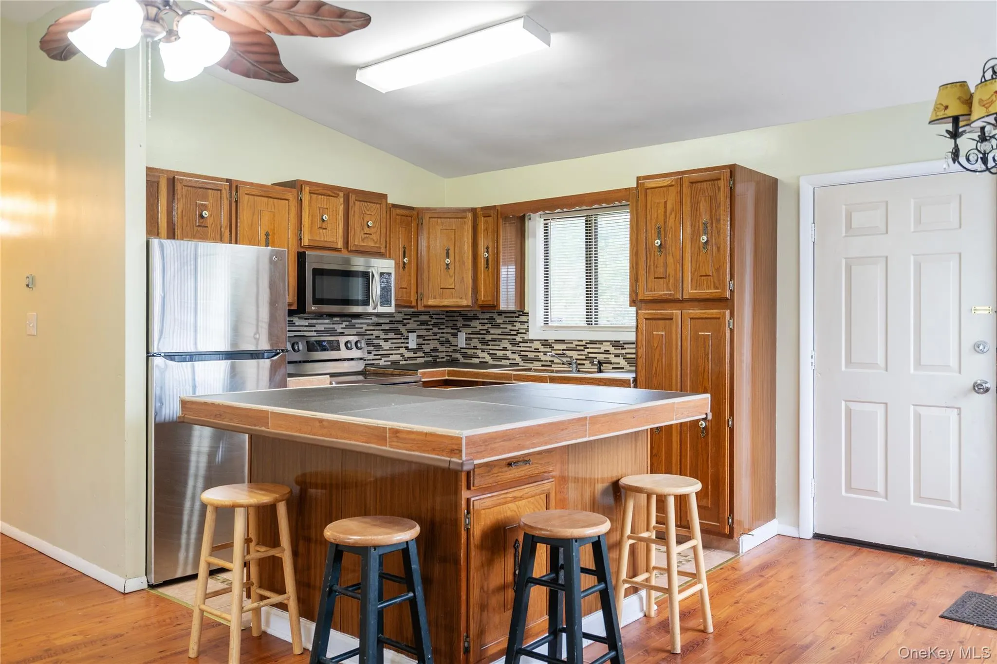 Kitchen with stainless steel appliances, tile countertops, lofted ceiling, tasteful backsplash, and brown cabinets Kitchen with stainless steel appliances, tile countertops, lofted ceiling, tasteful backsplash, and brown cabinets