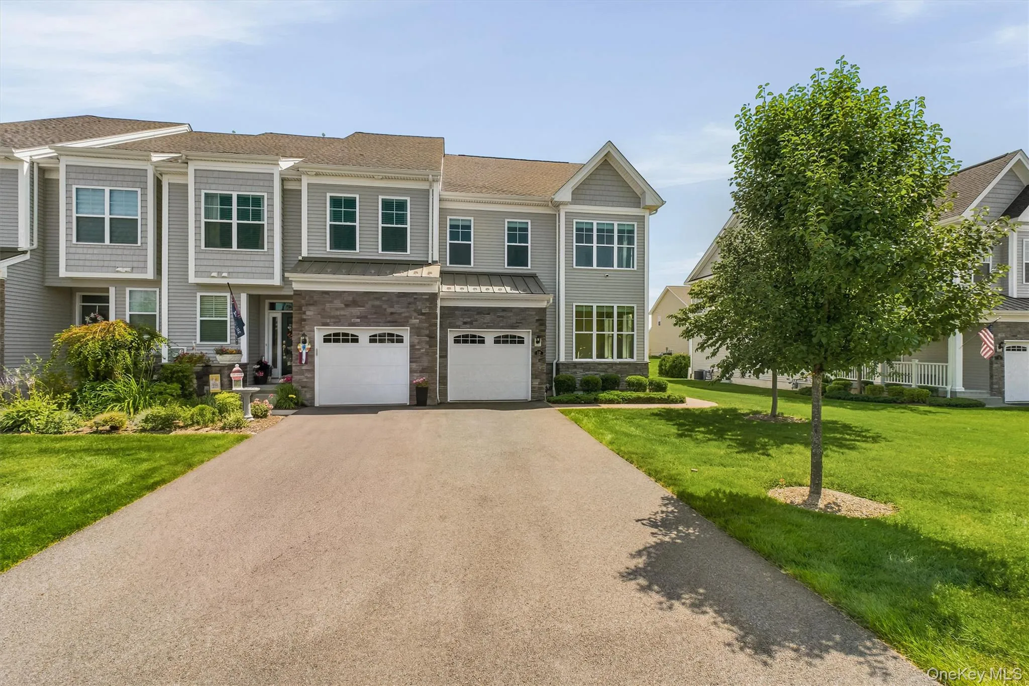 Townhome exterior featuring gray siding, stone facade accents, two-car garage, front landscaping, and a paved driveway Townhome exterior featuring gray siding, stone facade accents, two-car garage, front landscaping, and a paved driveway
