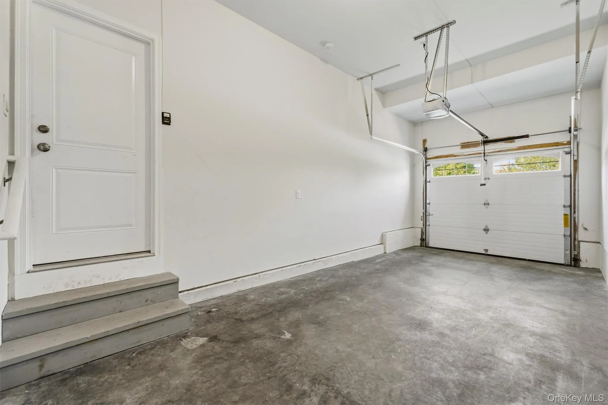 Spacious garage featuring a concrete floor, bright white walls, and a white overhead door with upper window panes Spacious garage featuring a concrete floor, bright white walls, and a white overhead door with upper window panes