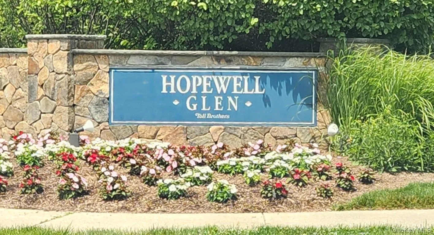 Stone entrance monument with integrated signage for "Hopewell Glen," featuring an established landscape bed with various flowering plants and ground cover. Stone entrance monument with integrated signage for "Hopewell Glen," featuring an established landscape bed with various flowering plants and ground cover.